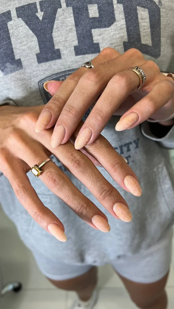 Close-up of a person's hands with manicured nails and rings, with a gray shirt with large letters in the background.