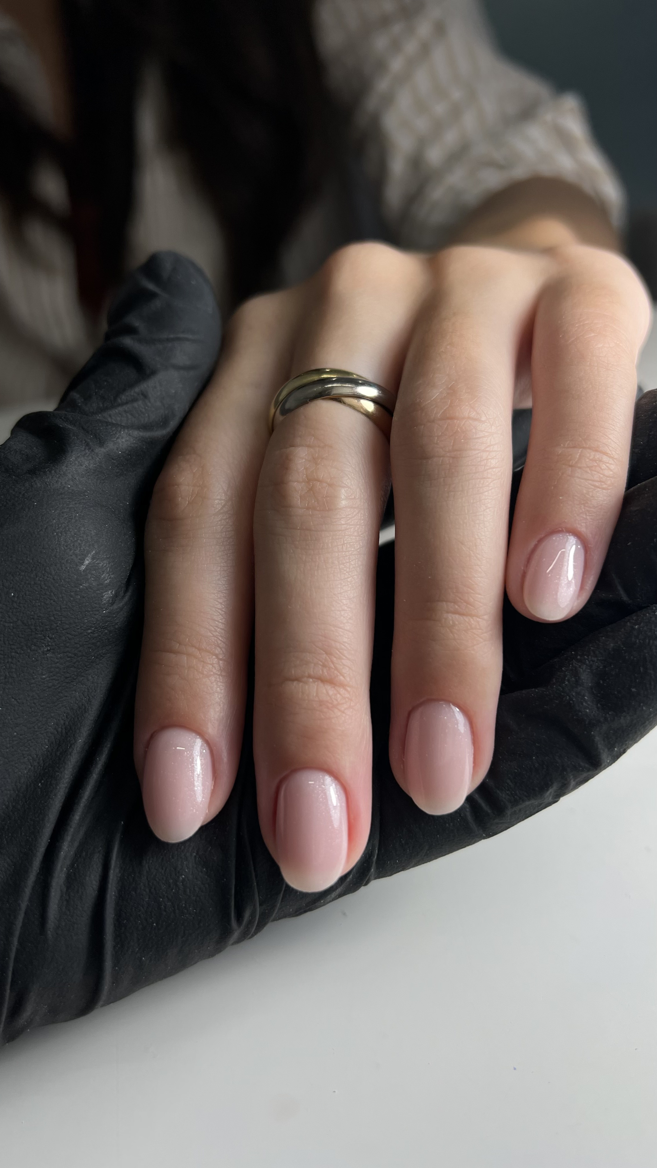 A hand with groomed nails wearing a gold wedding ring, holding a gloved hand.