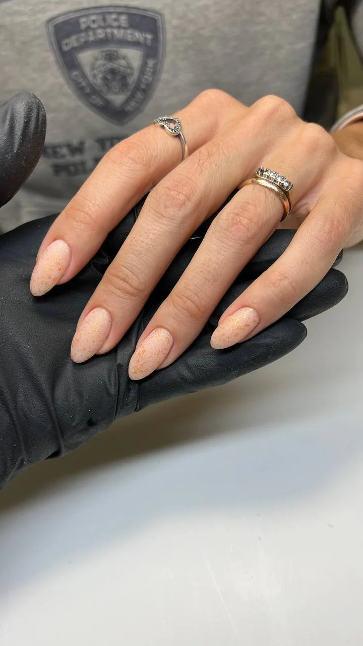 A person's hand with manicured nails and two rings, held by a person wearing a black glove. In the background, there is a police badge patch on a gray shirt.