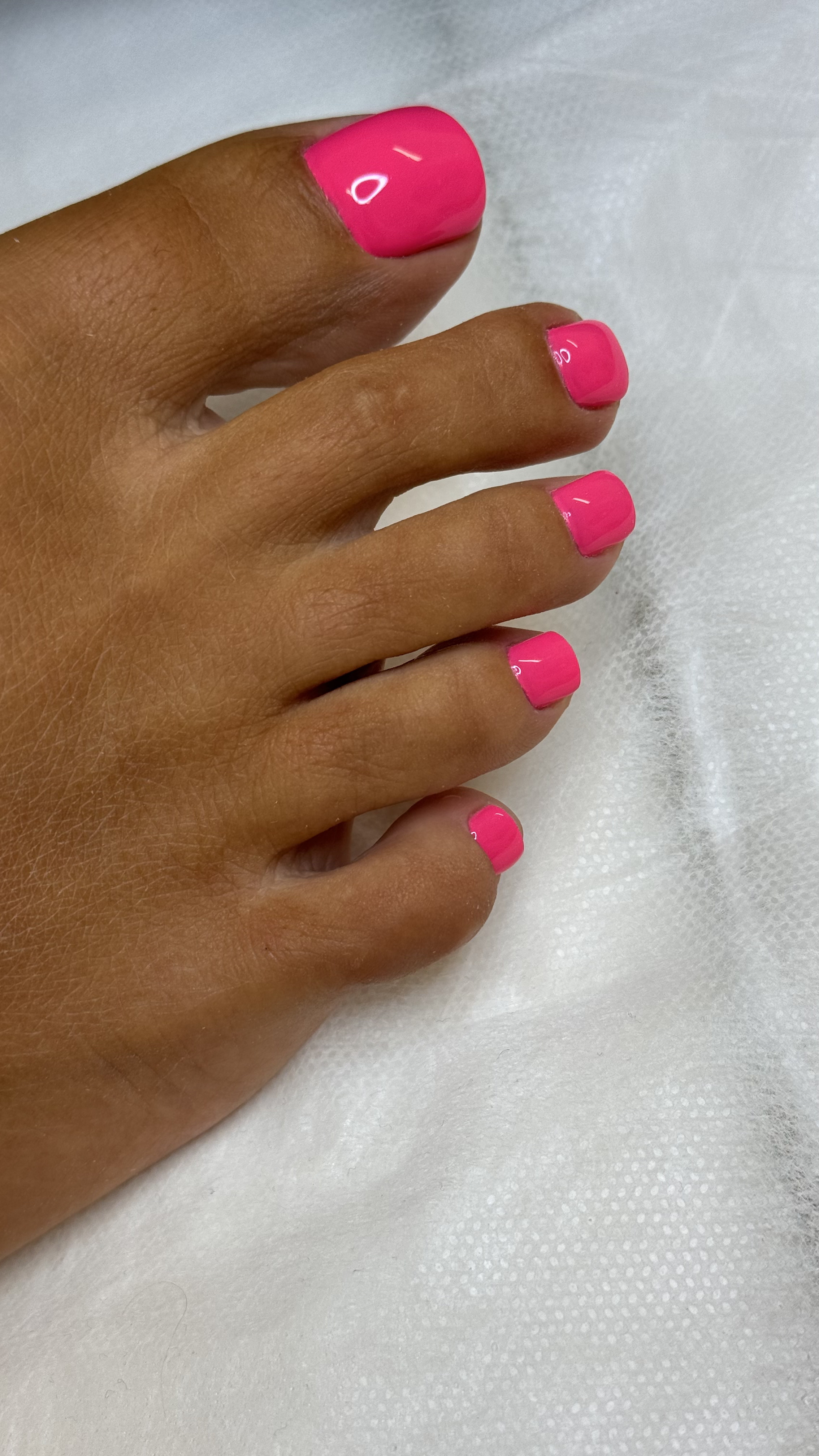 Close-up of a hand with neatly painted bright pink nails resting on a white textured surface.