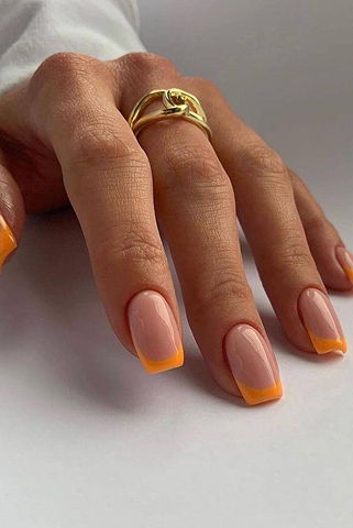 Close-up of a hand with orange-tipped natural nails and a gold ring on the middle finger.