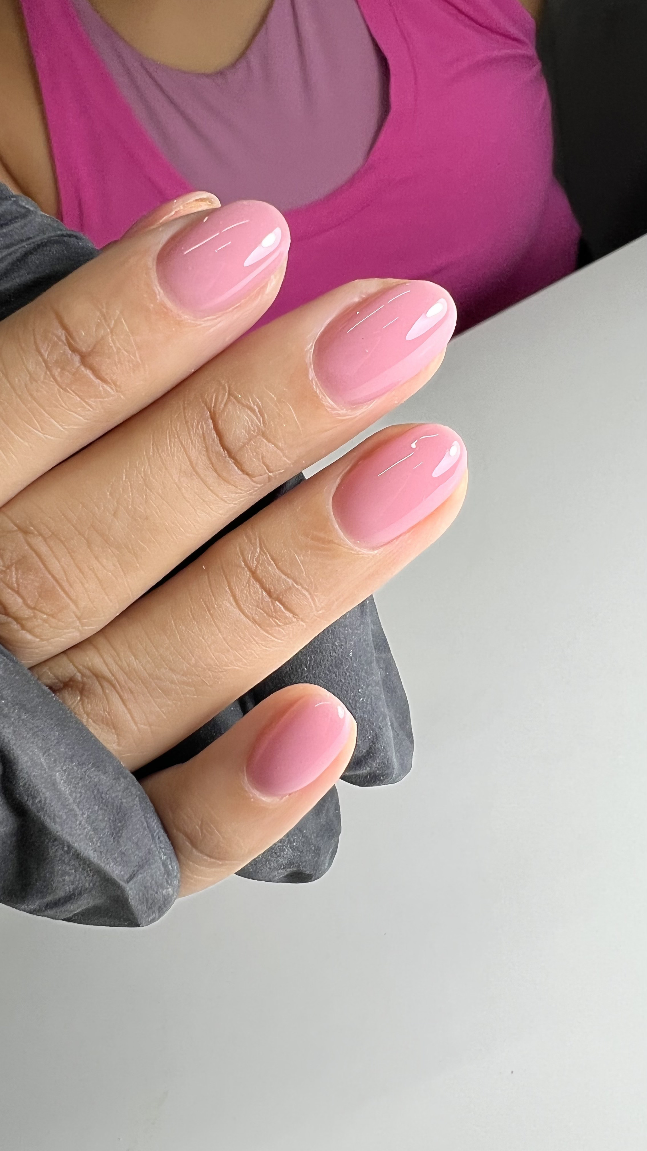 Close-up of a person's hand with short, oval-shaped nails painted in a natural pink gradient with a shiny finish.