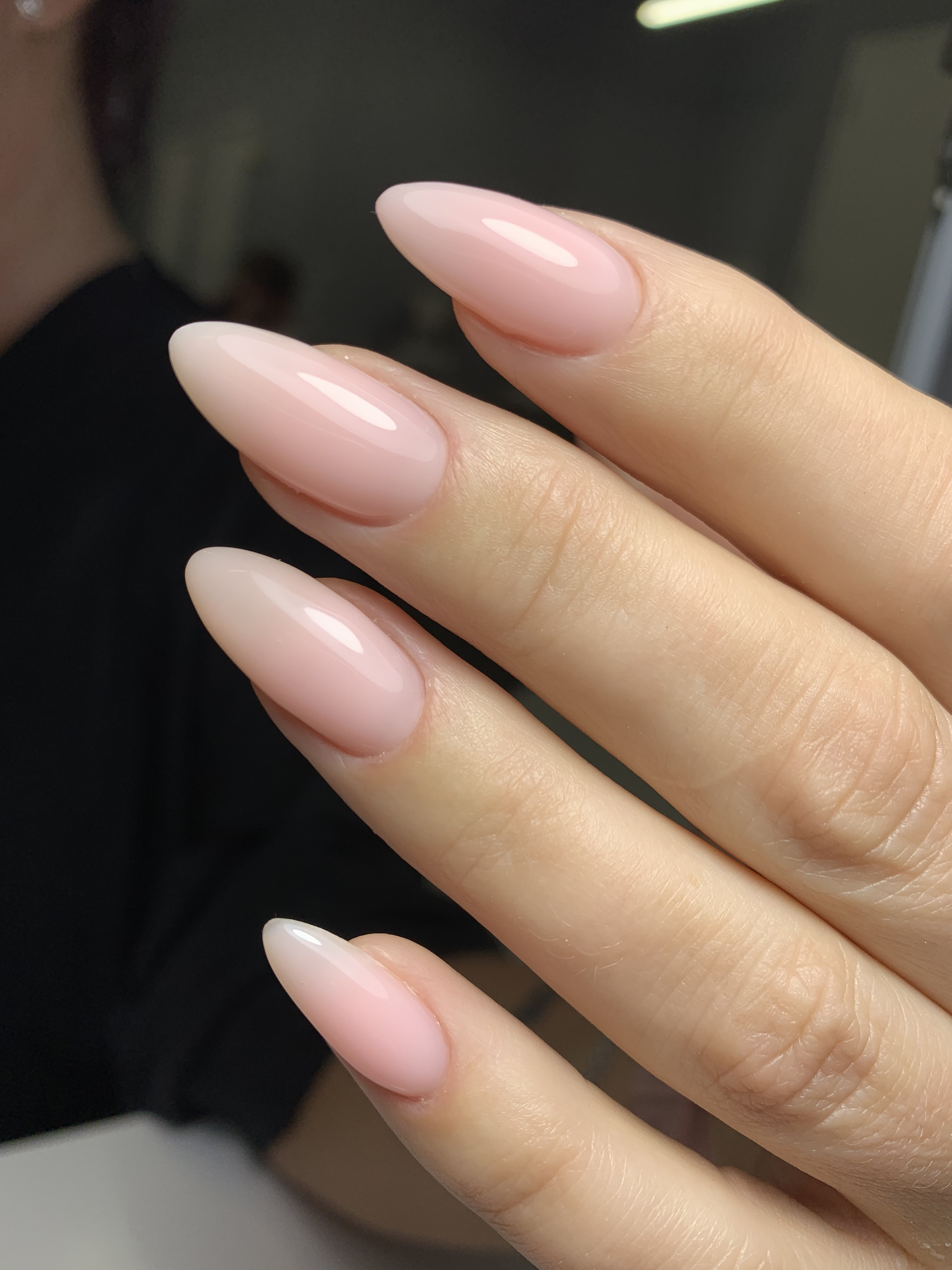 Close-up of well-manicured fingernails with pinkish-nude, glossy, almond-shaped nail polish.