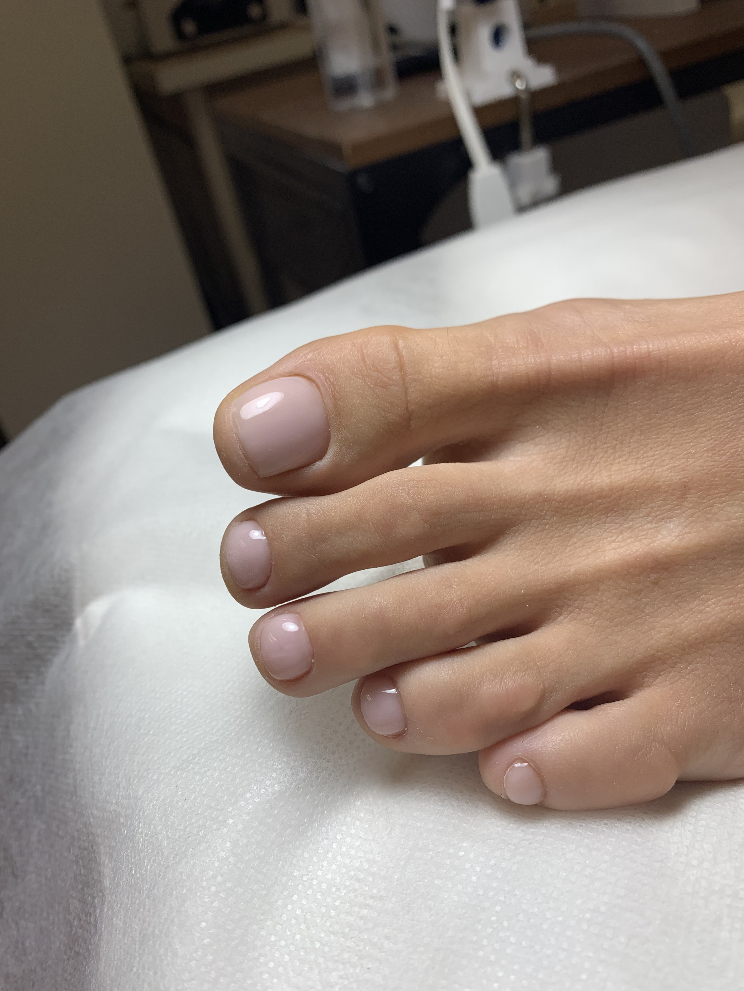 Close-up of a person's hand with neatly manicured, natural nails resting on a white cloth surface, with a blurred background of a workspace.