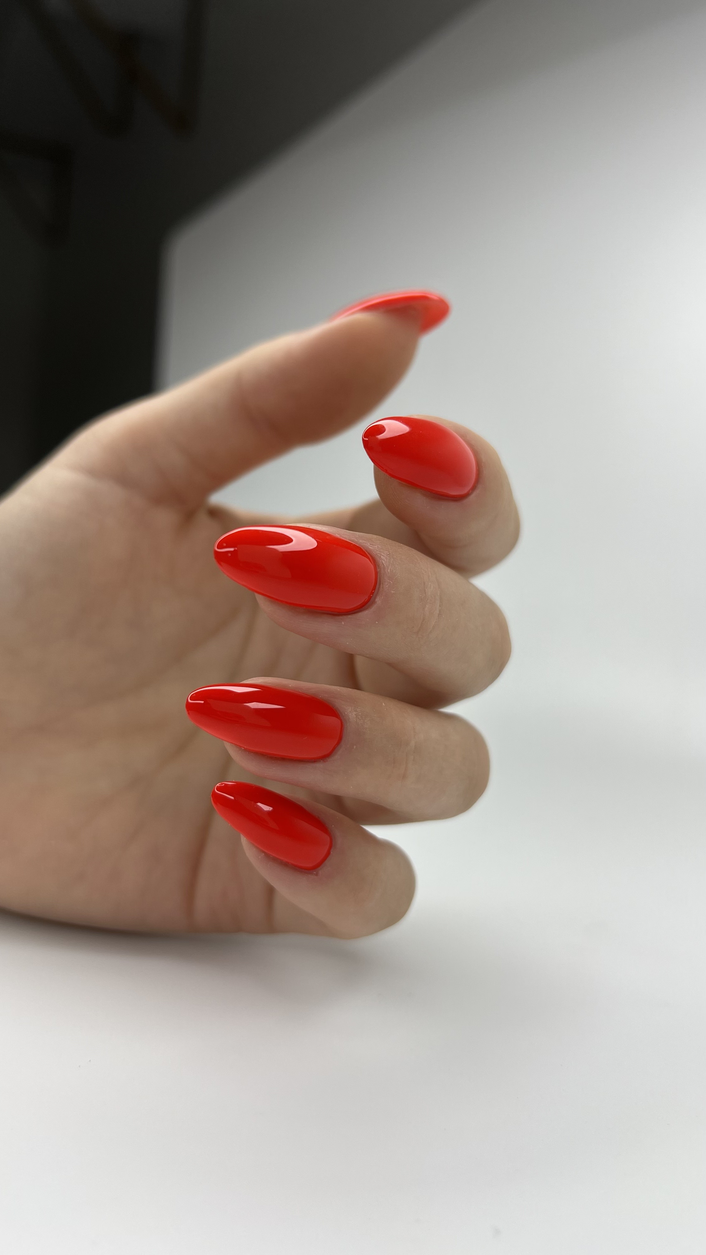 Close-up of a hand with long, glossy, bright red painted nails, with a white background.