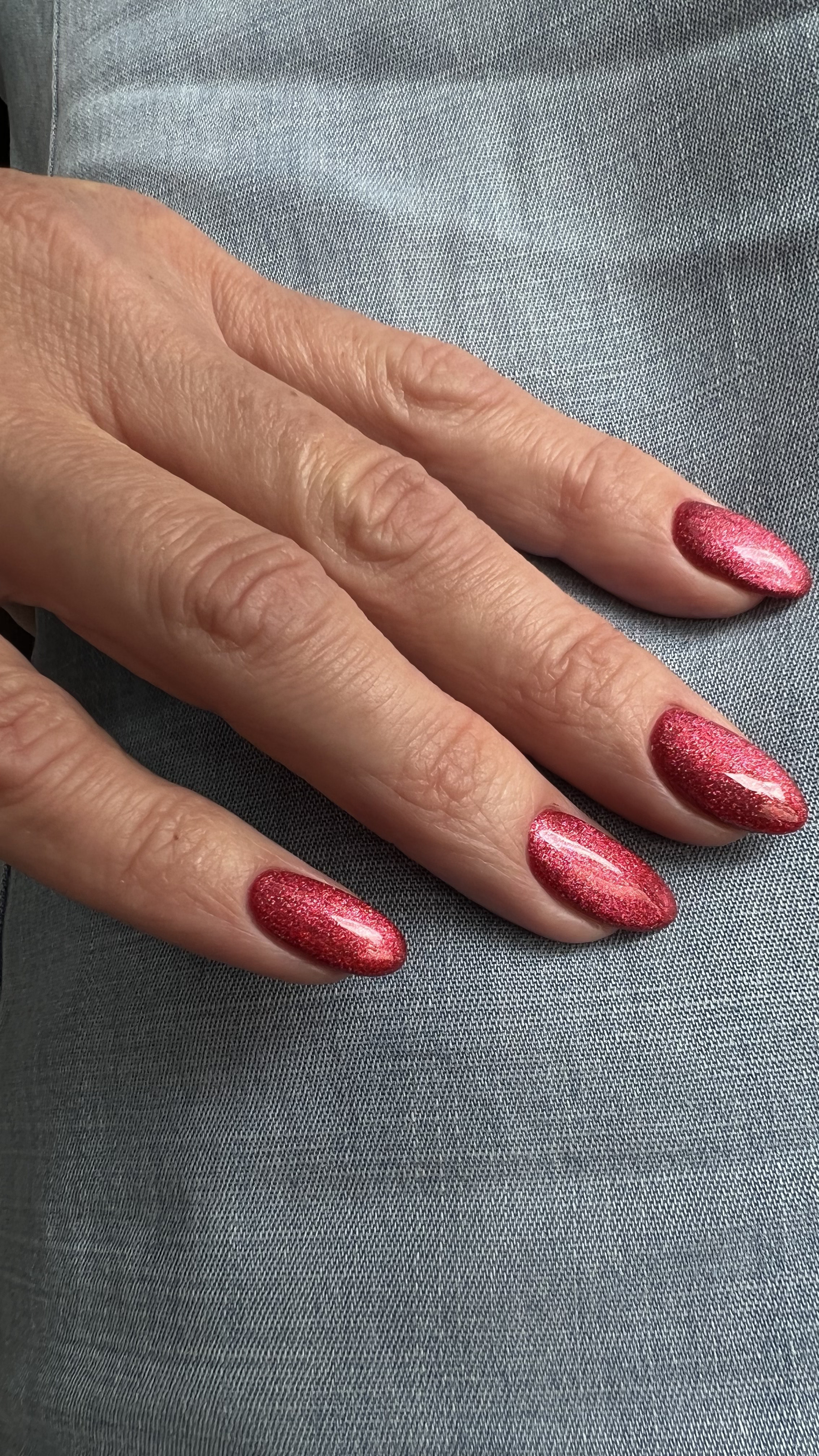 Close-up of a hand with pink metallic glitter nails resting on gray fabric.