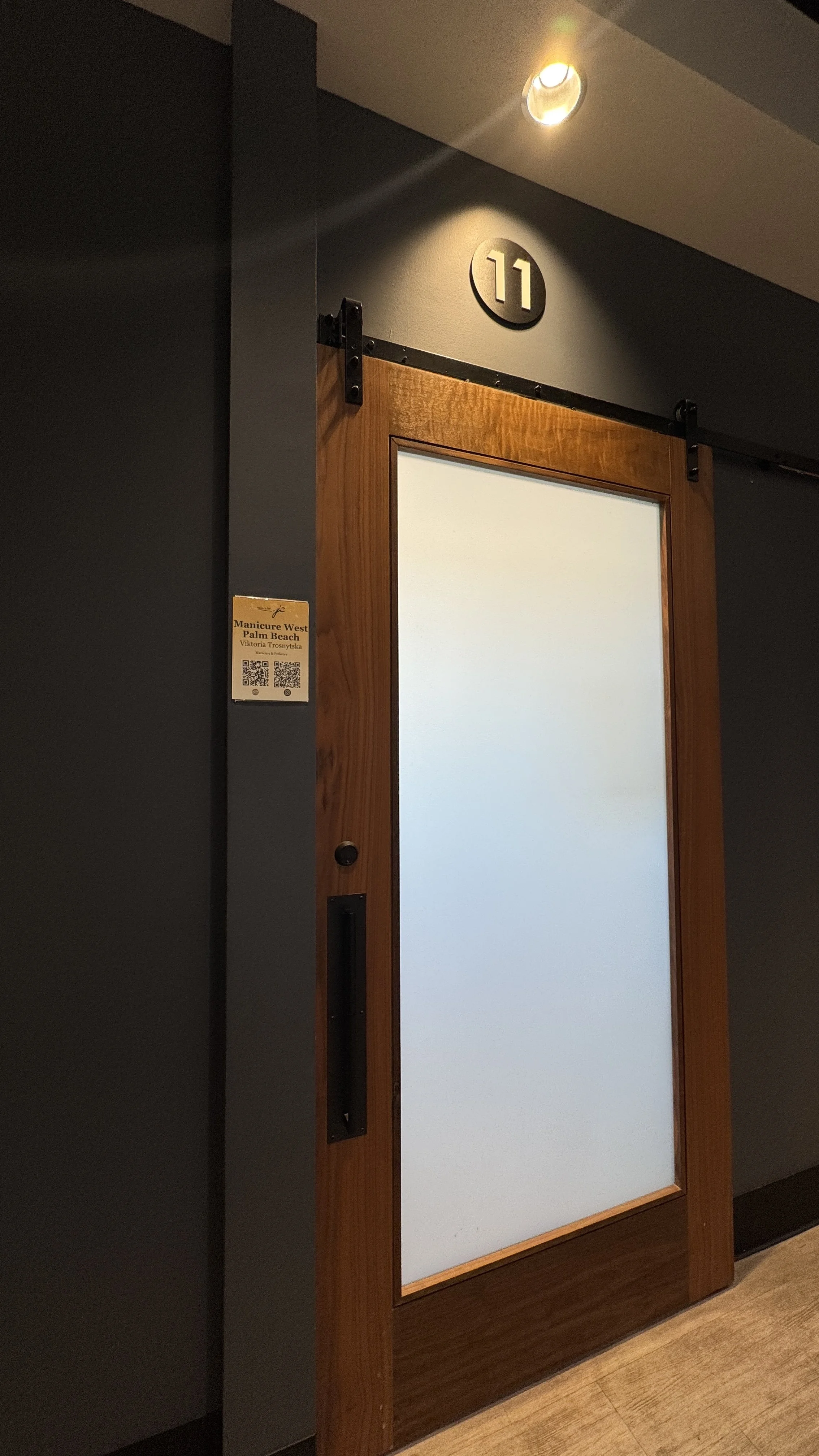 A wooden sliding door with a frosted glass panel, black hardware, and a black circular room number sign '11' above it, with a ceiling light illuminating the area.