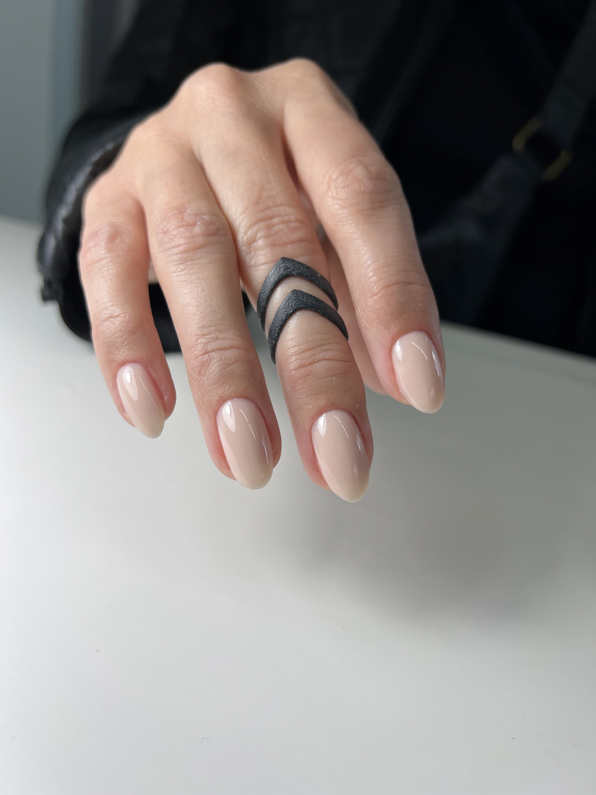 Close-up of a hand with four black crescent-shaped rings on the middle finger, displaying neatly manicured nails with nude polish.