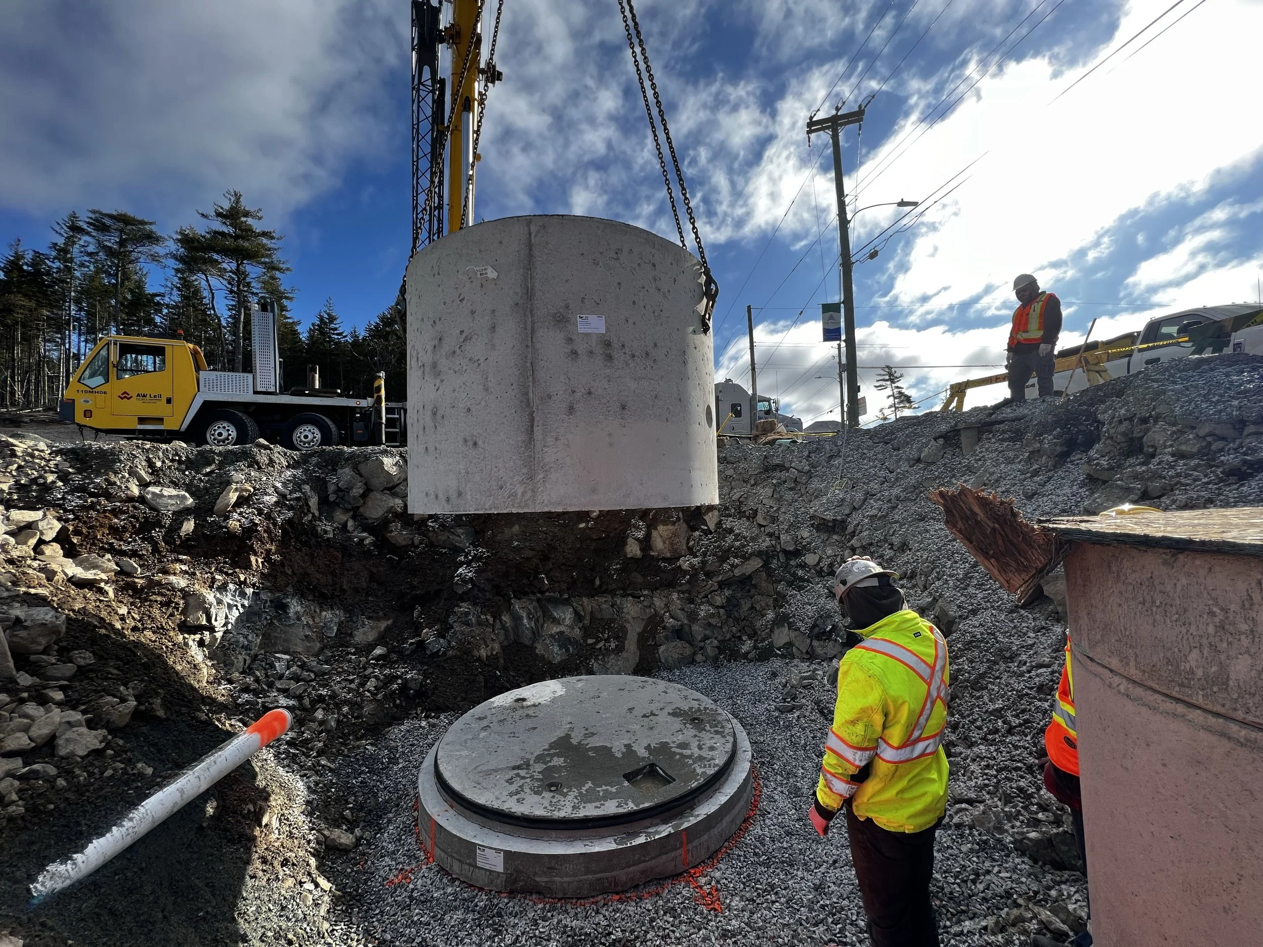 Construction workers in safety gear monitor large concrete structures being installed at a construction site, with heavy machinery and utility poles in the background.