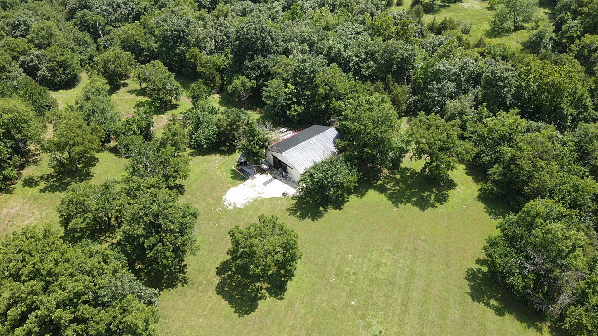Aerial view of a rural property with a large shed surrounded by trees and open grassy area.