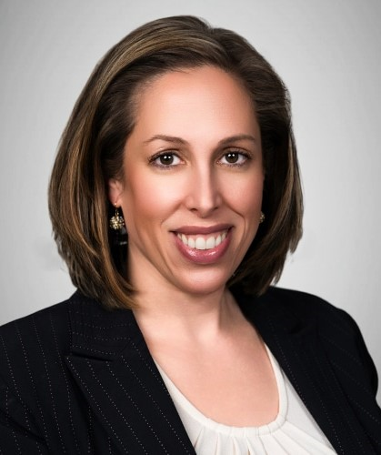 Professional woman with shoulder-length brown hair, wearing a black pinstripe blazer and a white top, smiling against a neutral background.