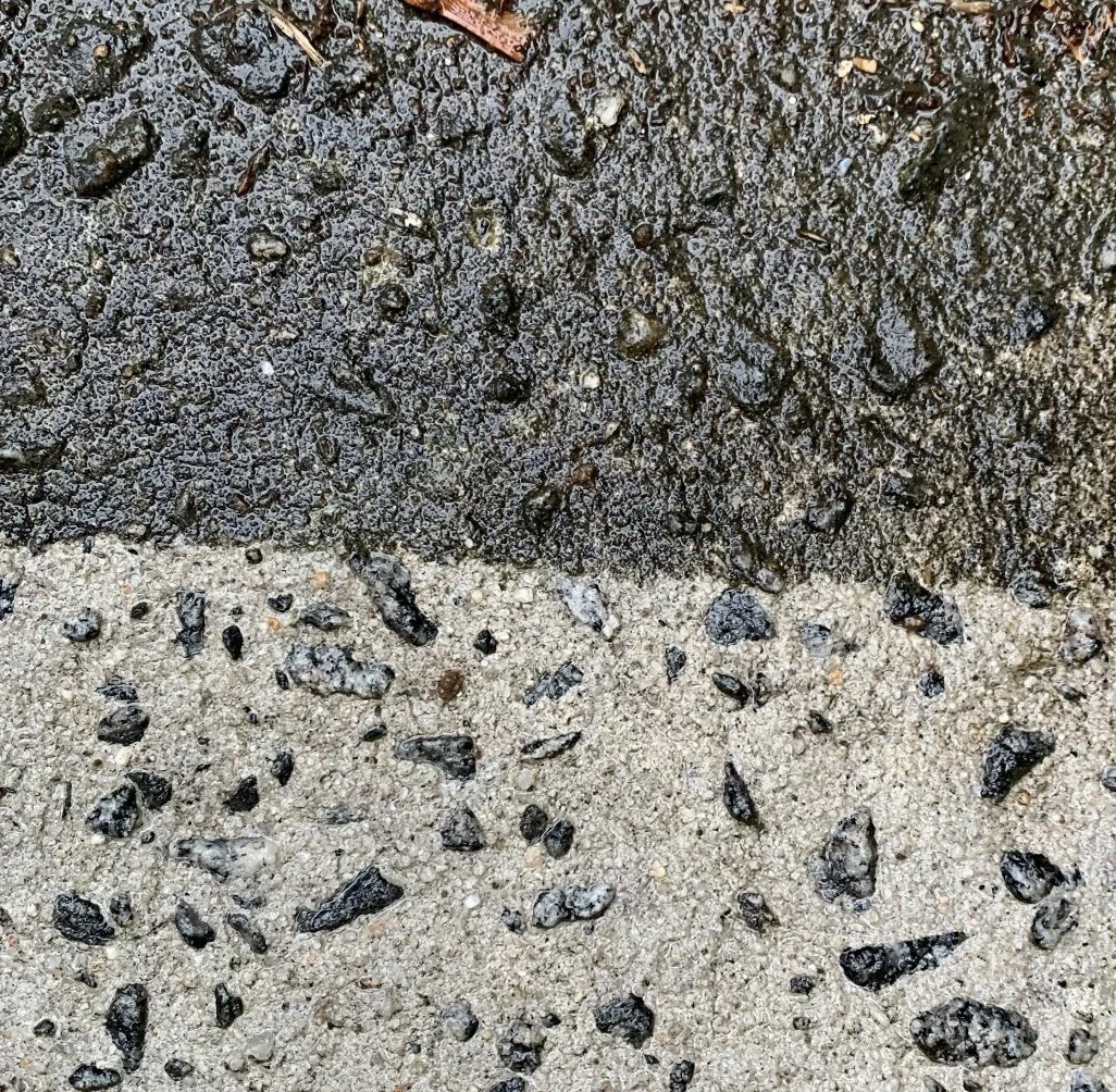 Close-up photo of two different types of asphalt or concrete pavement, one dark and rough, the other lighter with small stones, separated by a faint line.