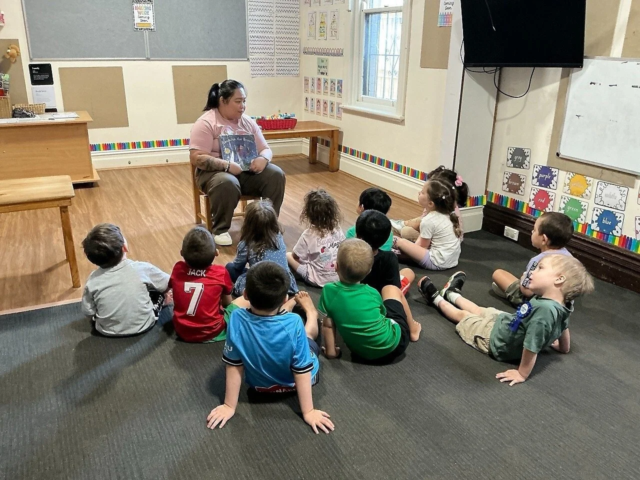 Teacher reading a book to young children seated on the floor in a classroom.
