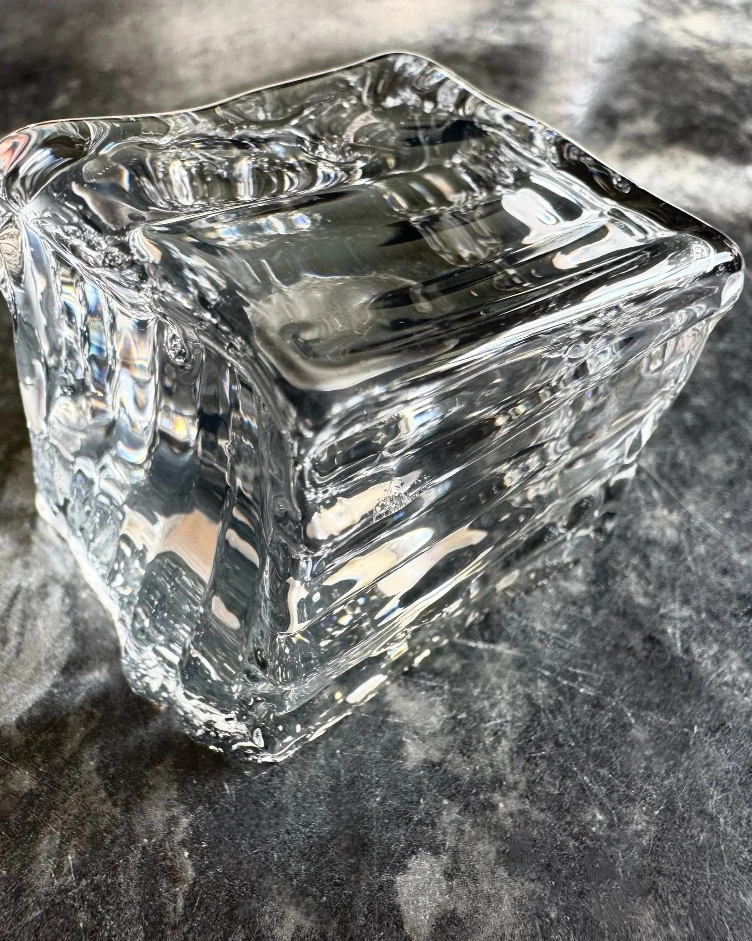 Close-up of a clear glass ice cube on a dark surface.
