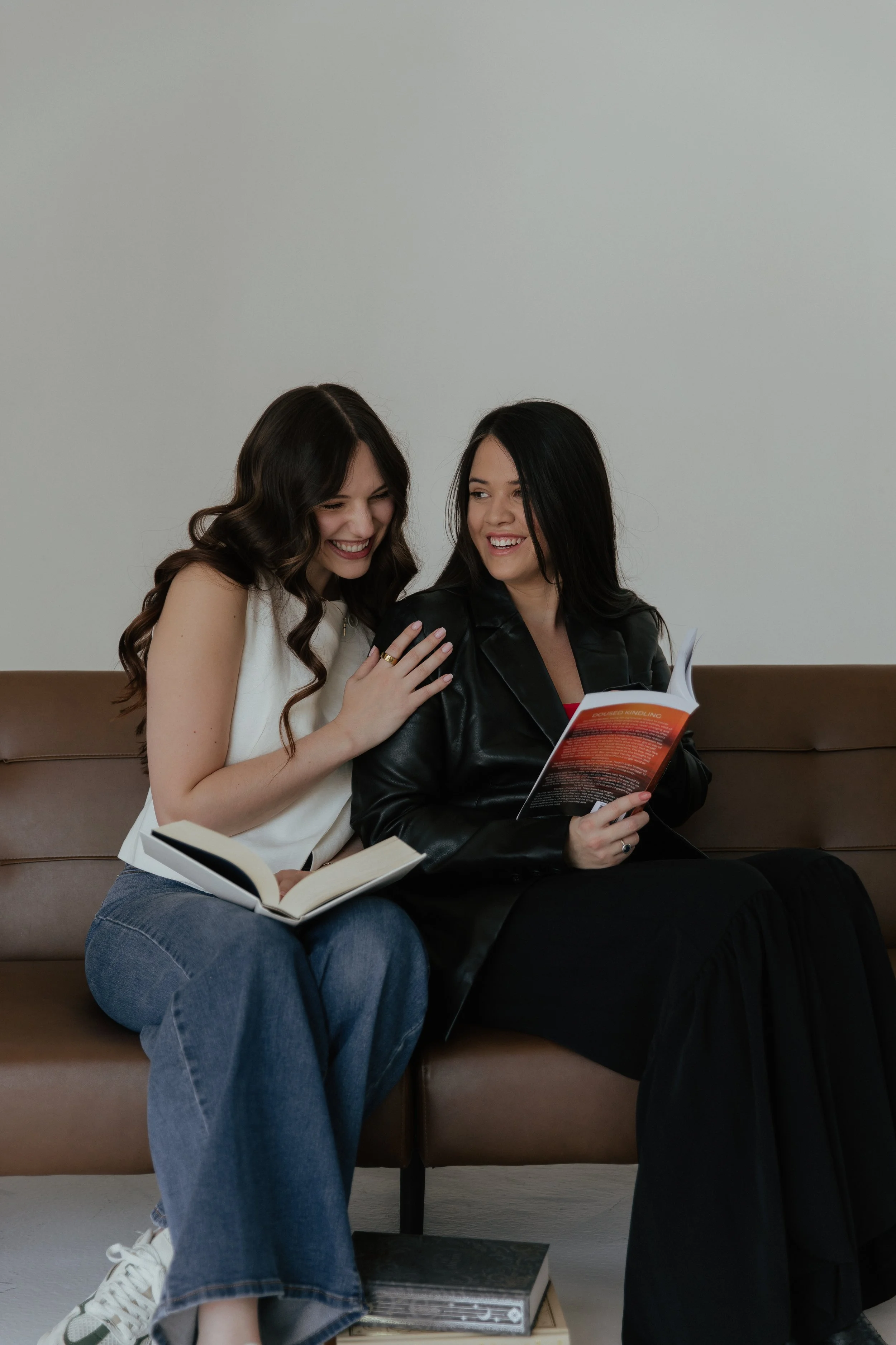 Two women sitting on a bench, sharing a moment of laughter while looking at a book.