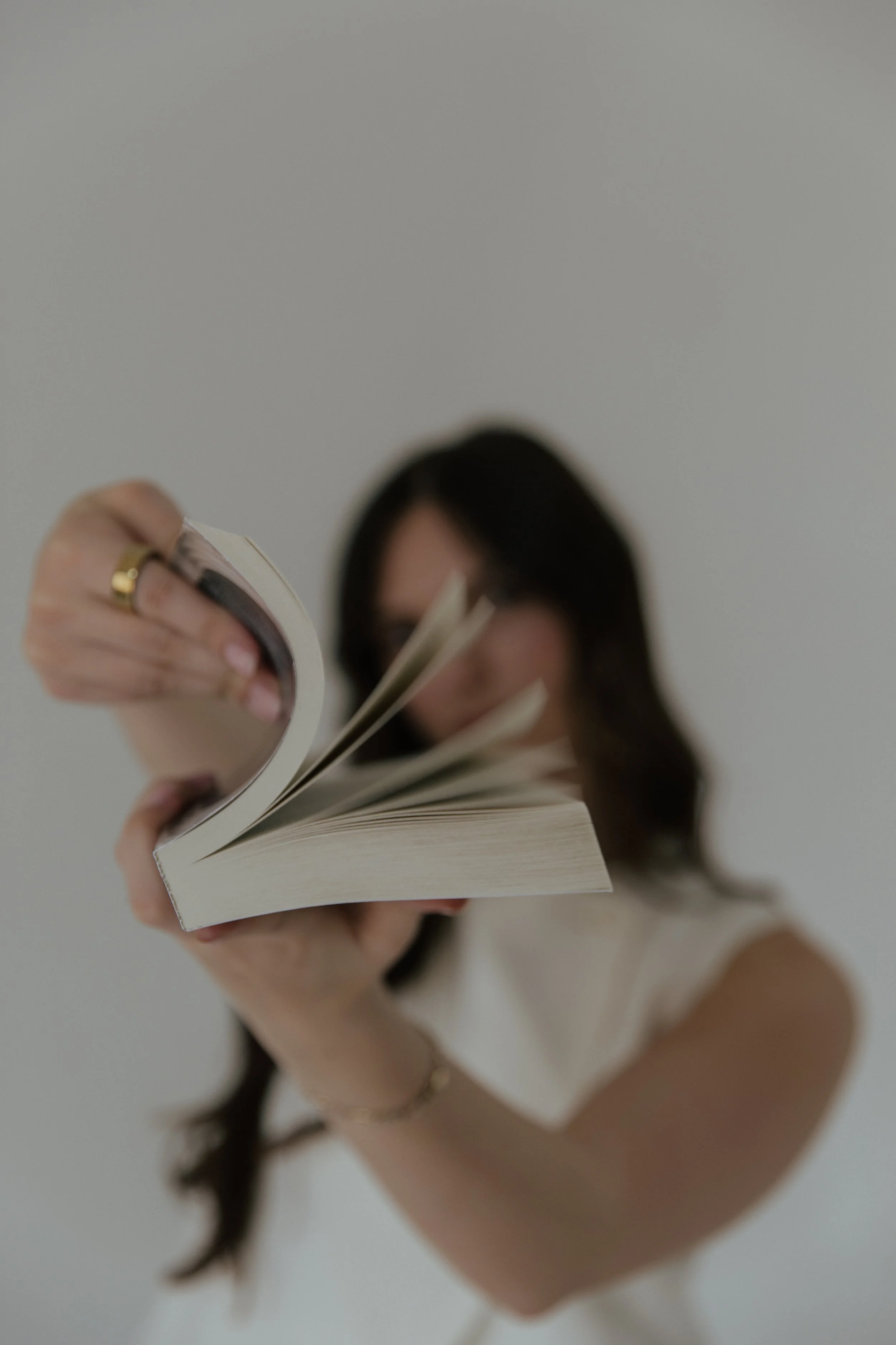 A person holding a book open, with long dark hair visible, against a plain gray background.