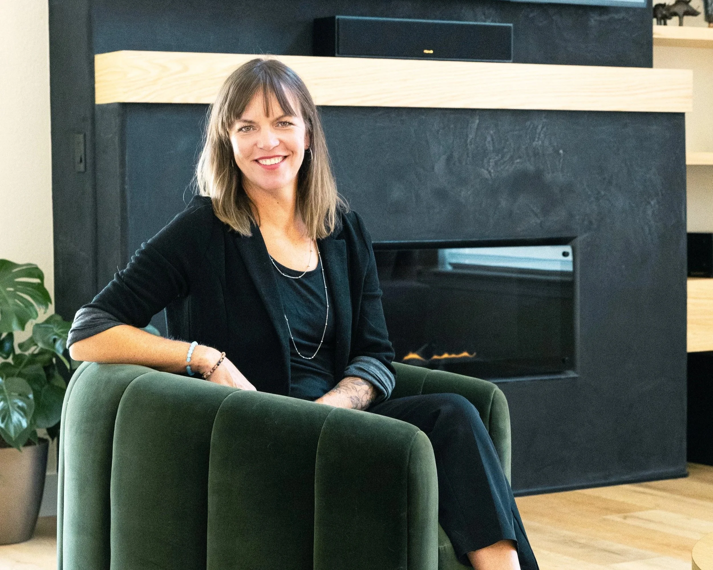 A woman with shoulder-length brown hair sitting on a green armchair in a modern living room.