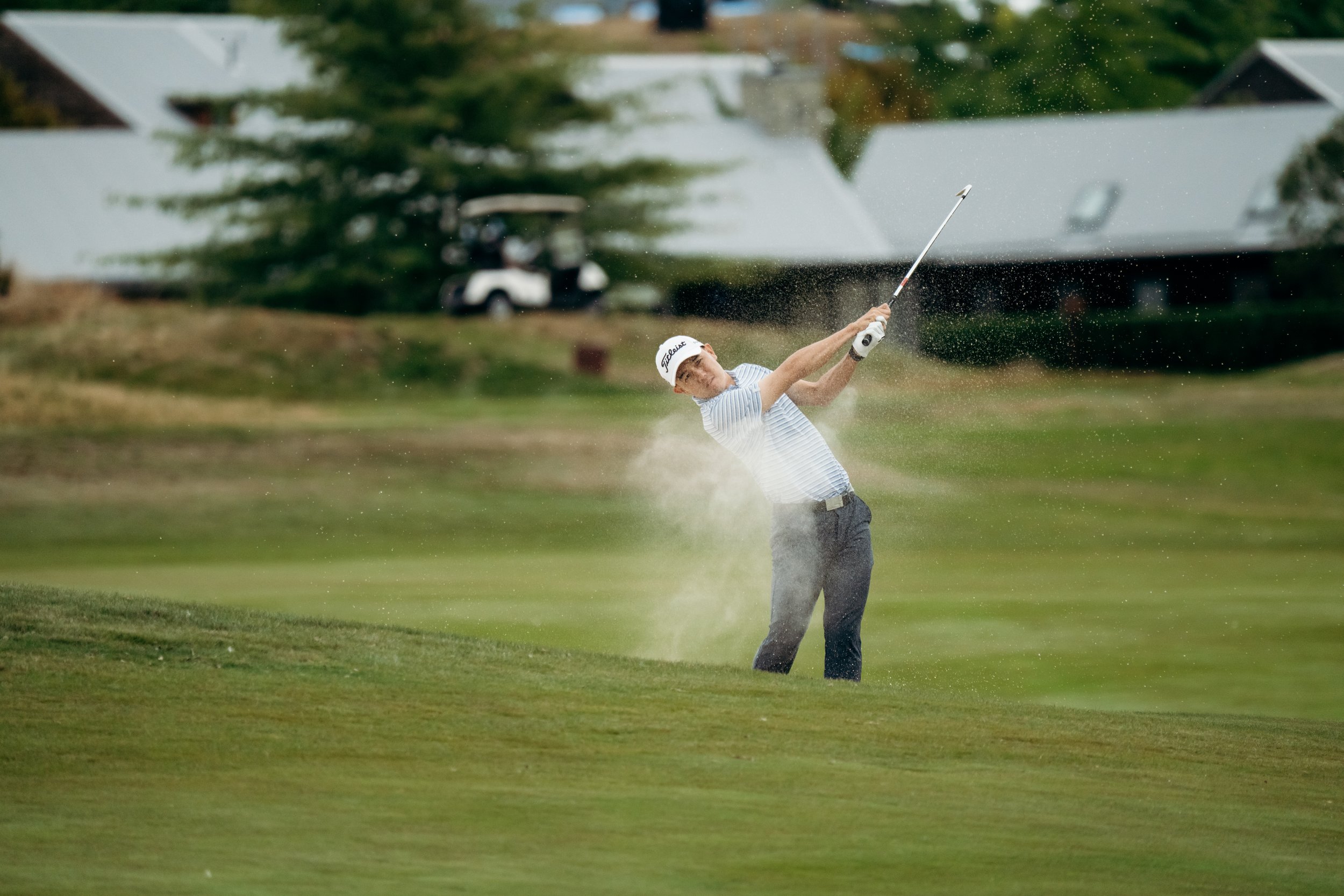 A man taking a golf shot from a sand trap on a golf course.