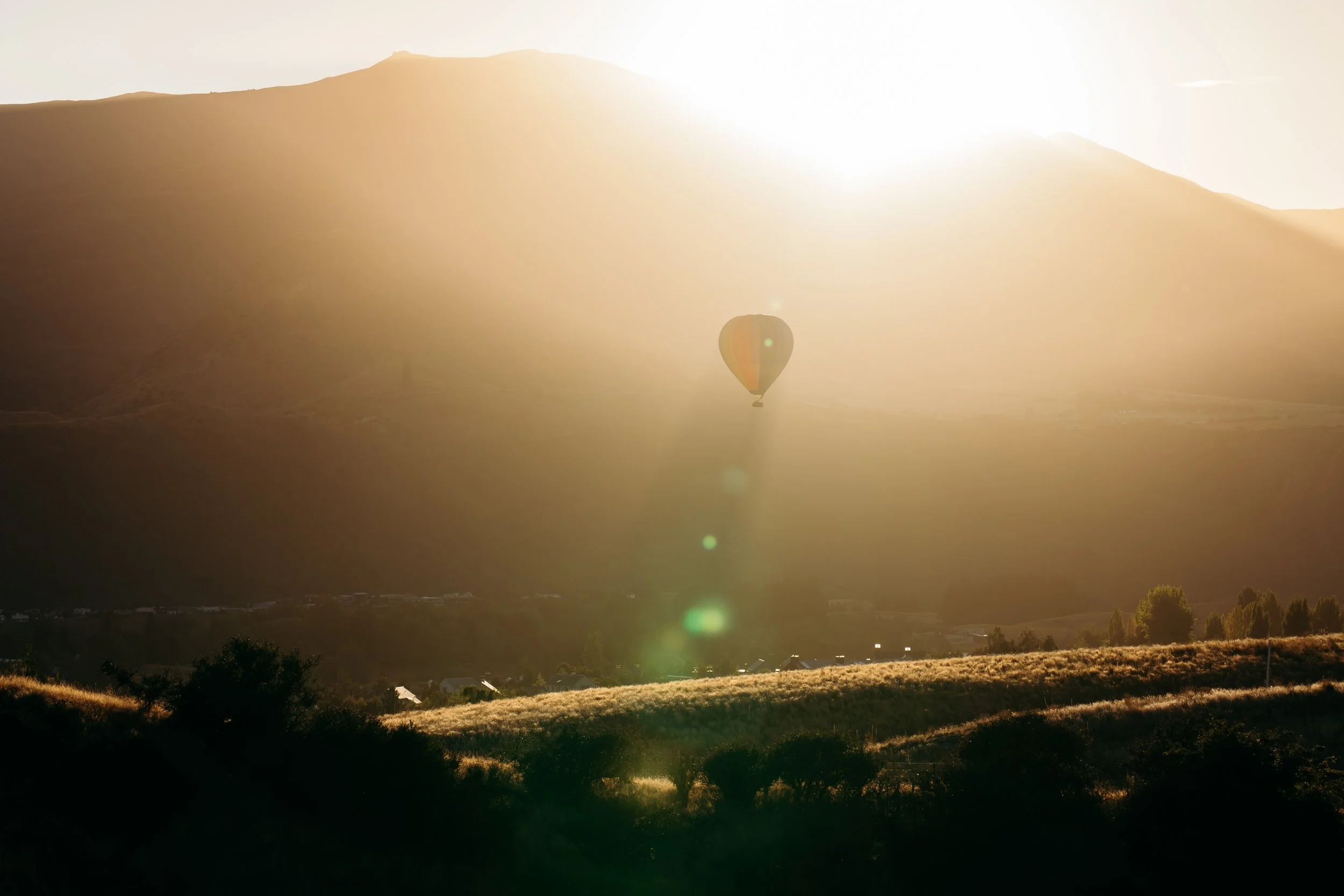 A hot air balloon floating in the sky during sunrise over a landscape with hills and trees.