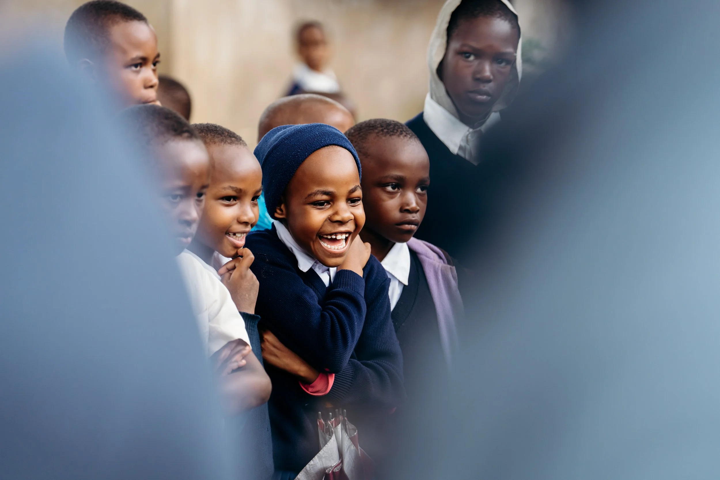 Group of children standing together, some smiling and others with serious expressions, in an indoor setting.