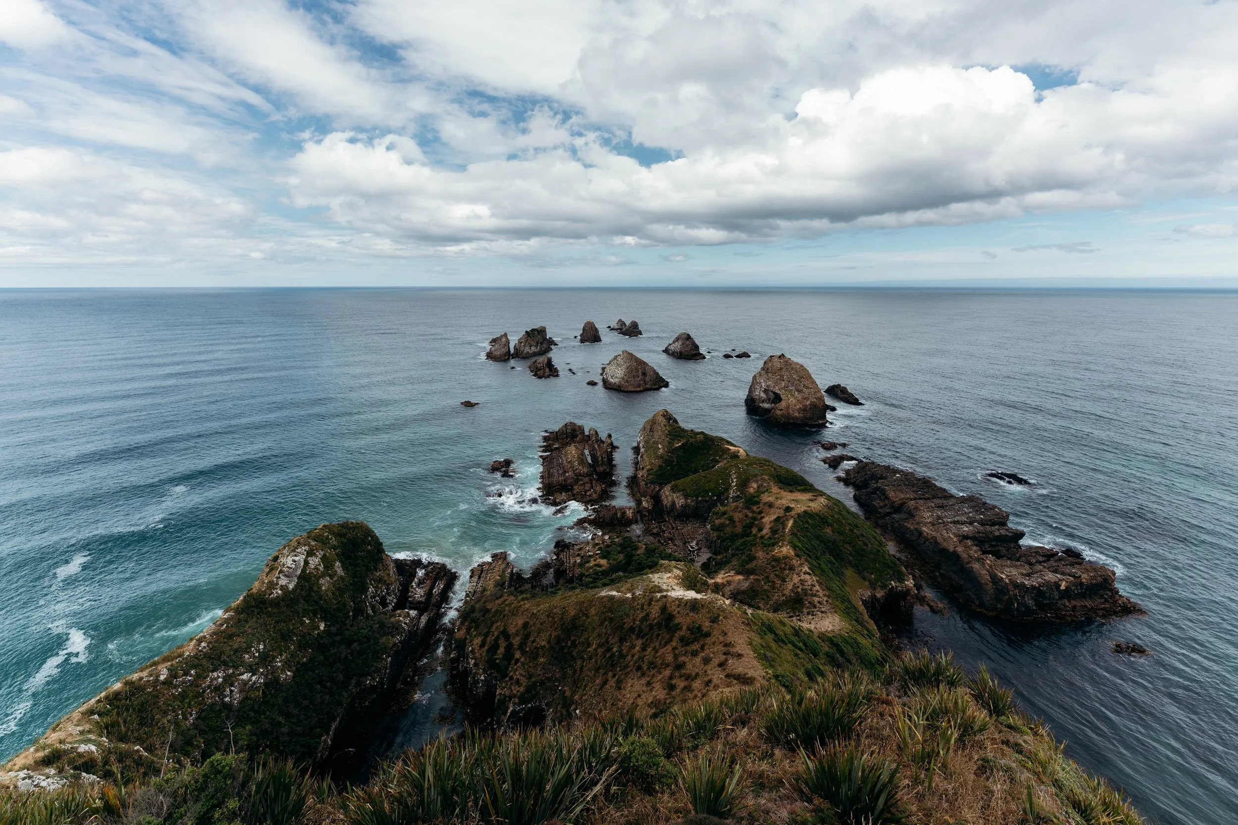 Cliffside view of rocky shoreline and ocean with partly cloudy sky.