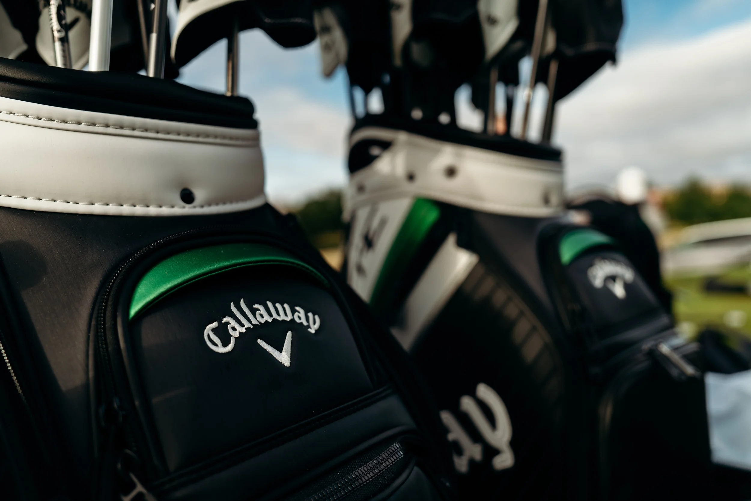 Close-up of golf clubs stored in a golf bag, with a visible Callaway golf ball pocket, set against a sky background.