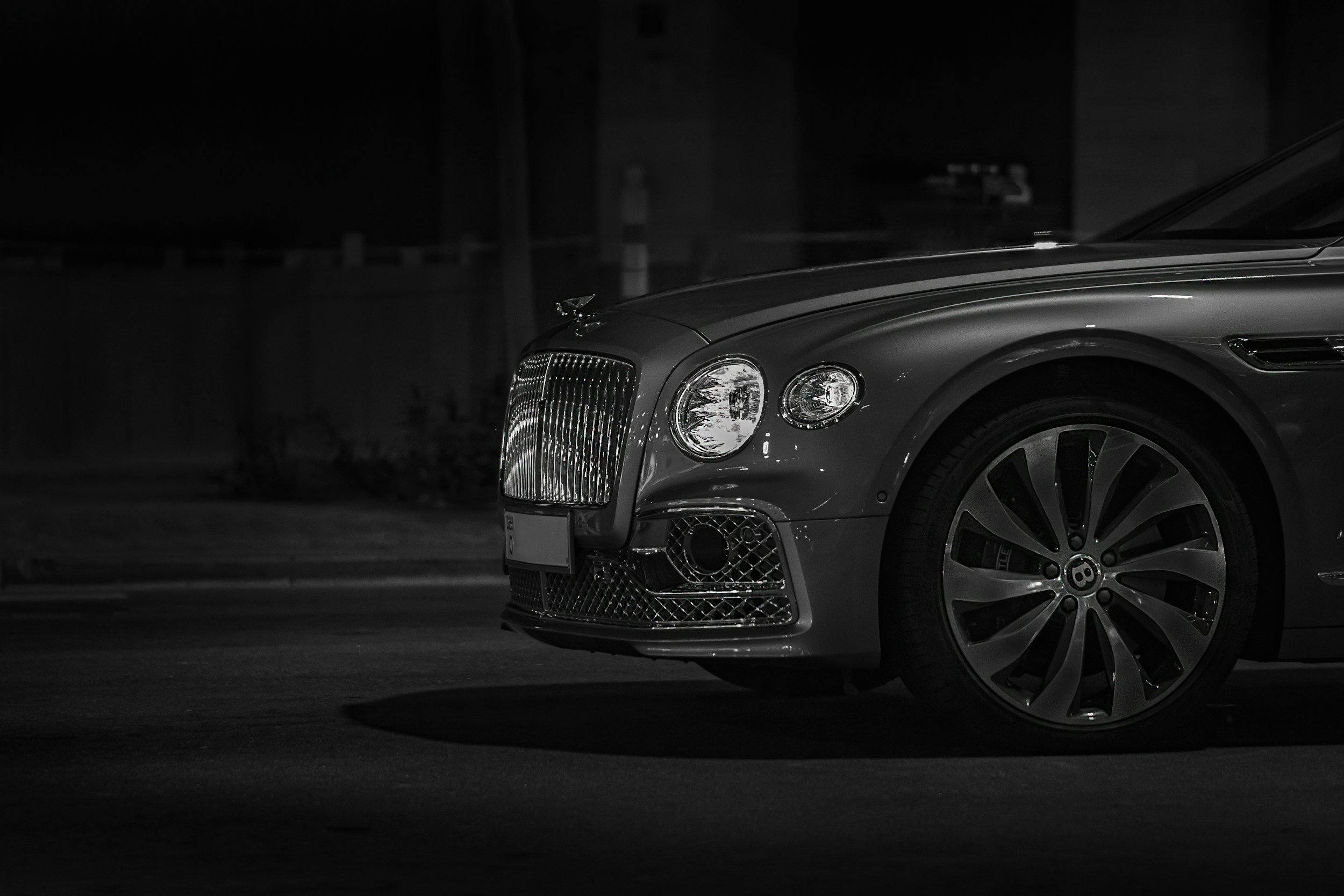 Close-up of the front part of a luxury gray Bentley car parked in a dark area.