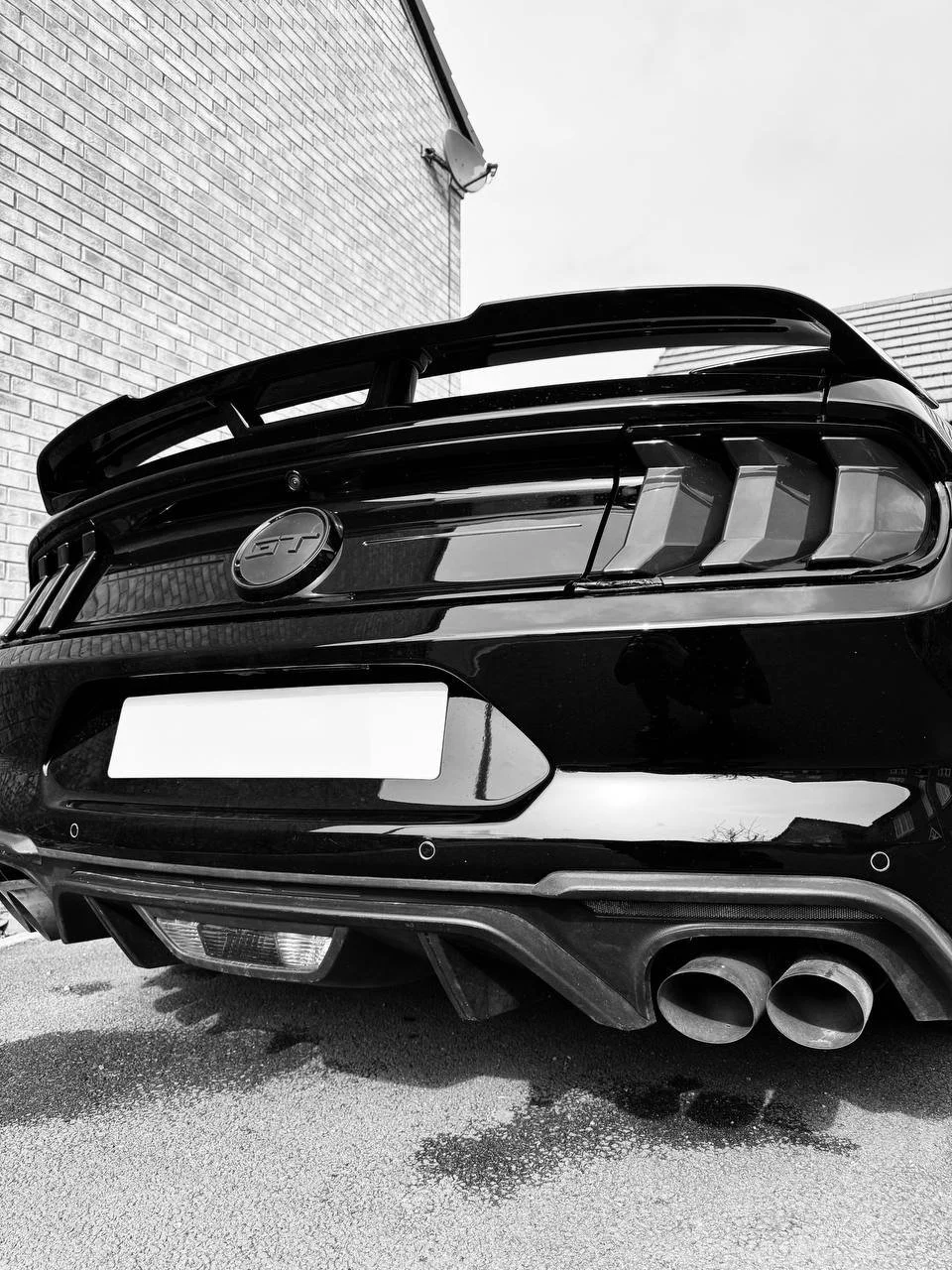 Rear view of a black sports car with GT badge, double exhaust pipes, and aerodynamic rear spoiler