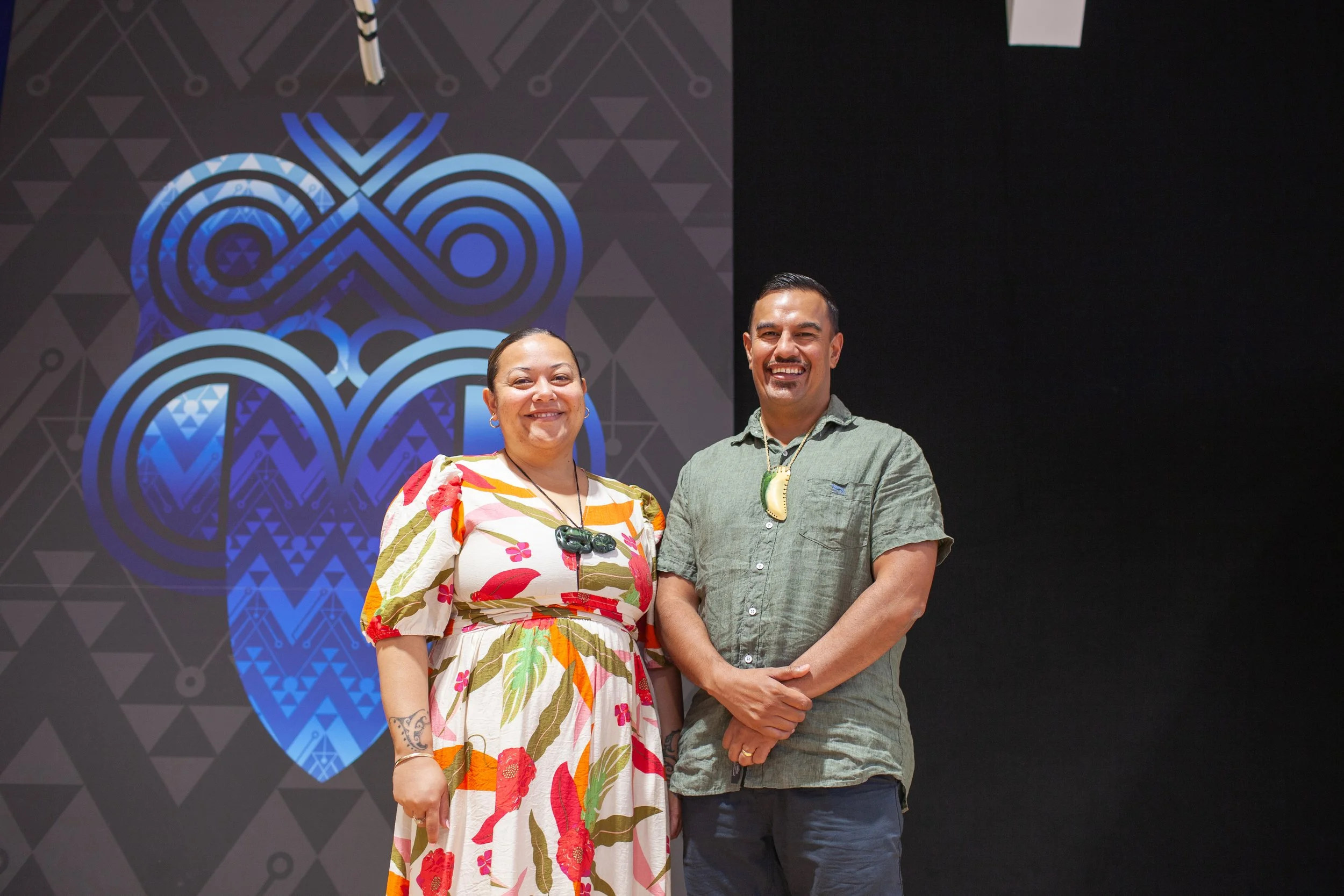 A man and woman standing together smiling in front of a graphic artwork with blue and black geometric patterns.