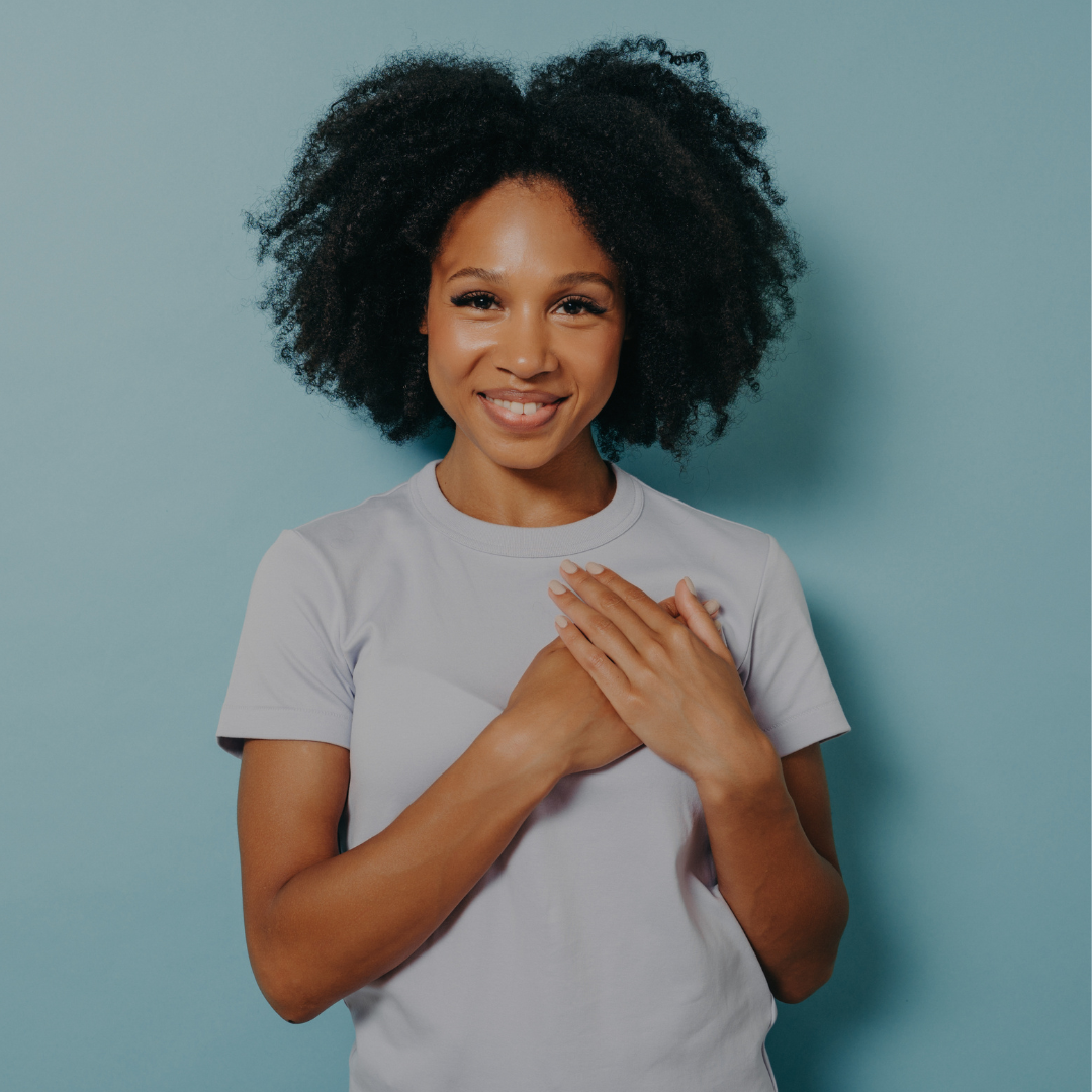 Woman smiling holding both hands over her heart on Reclaiming_HER_Resilience_website