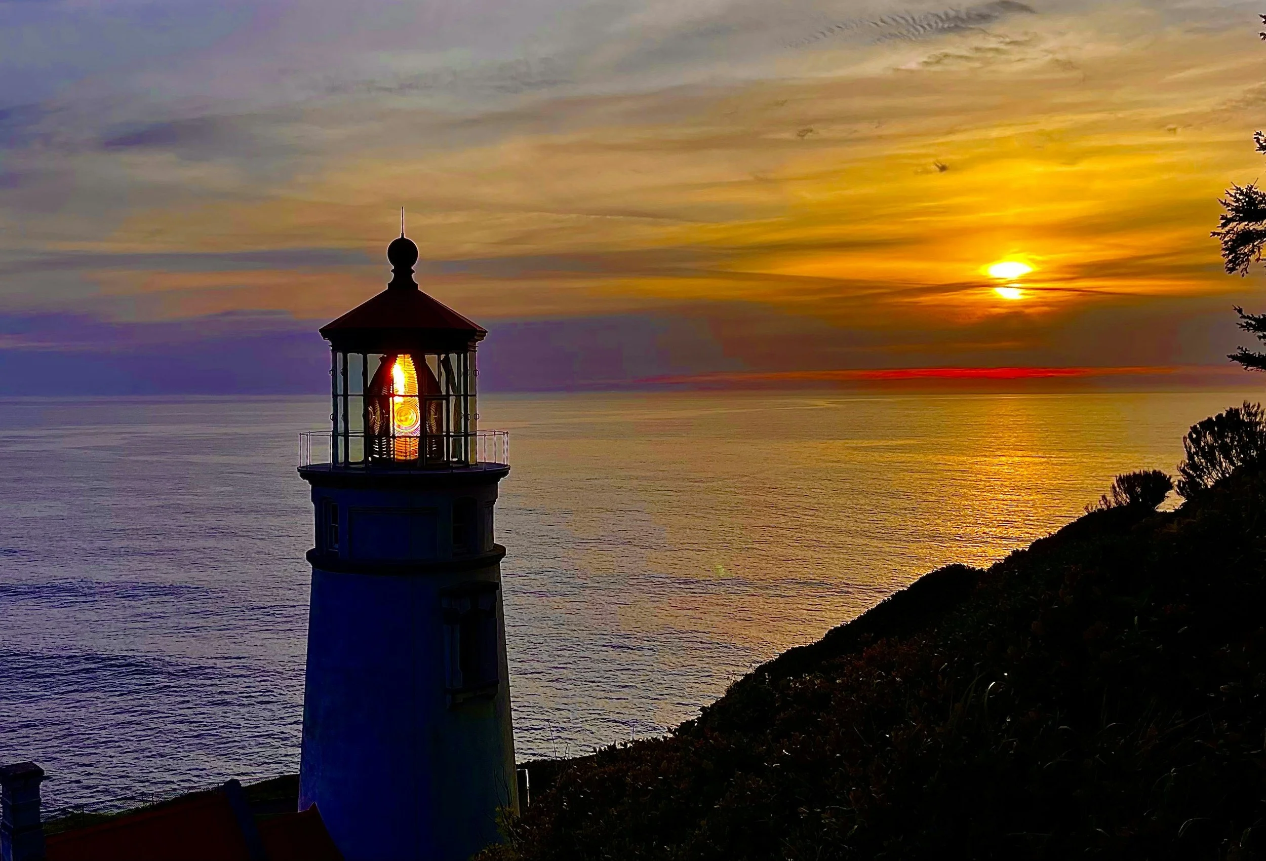 The top of  lighthouse with the light on as the sun sets