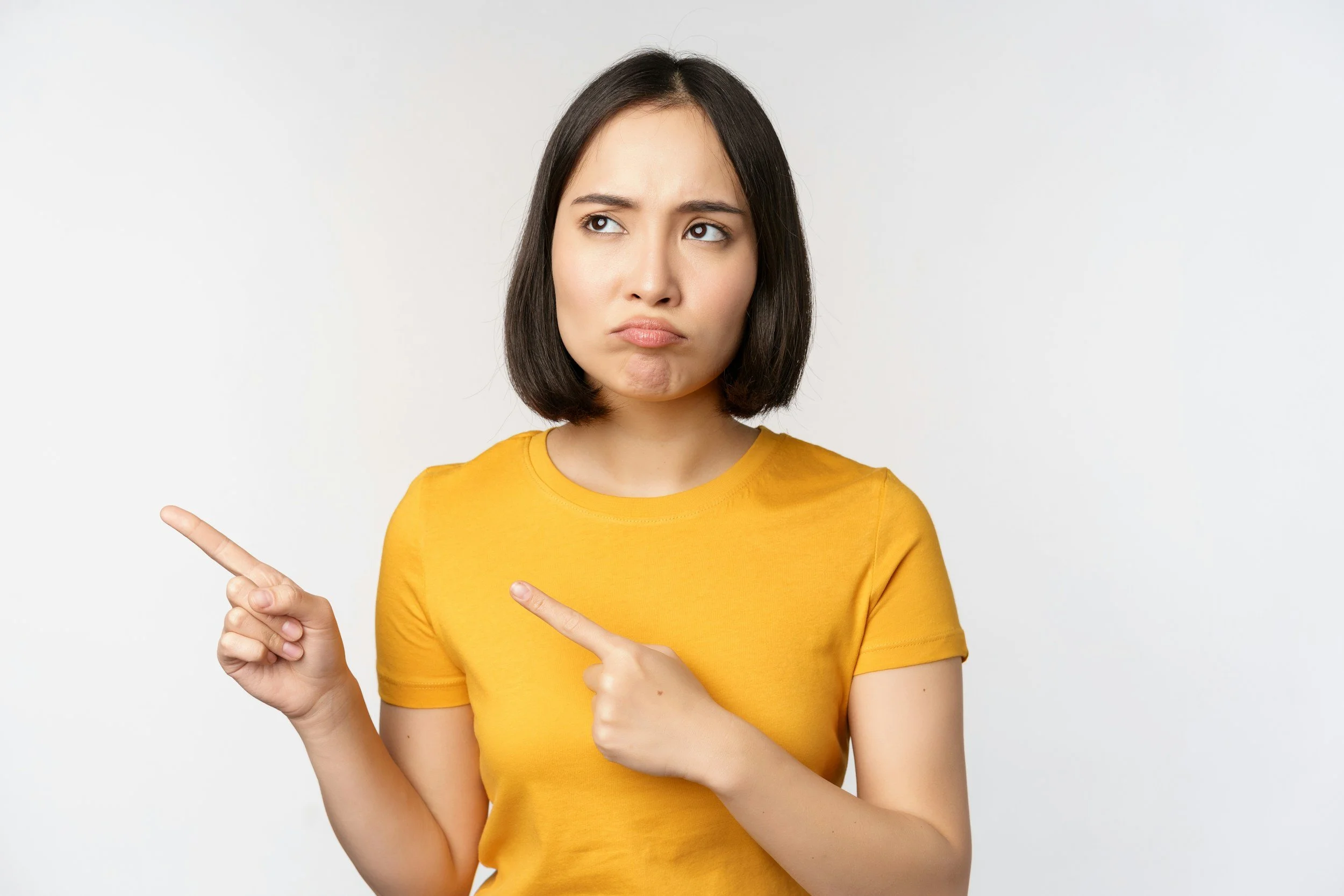 A woman looking upward and to the side unsure with both index fingers pointing to the left.