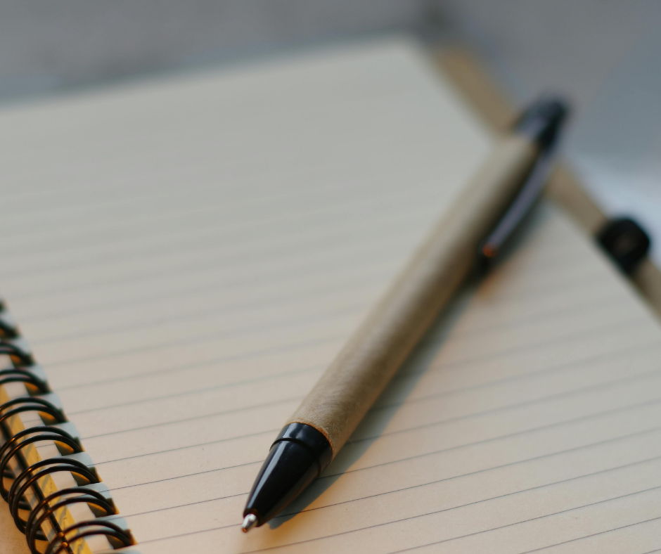 Close-up of a black ink pen resting on an open, lined, spiral notebook.