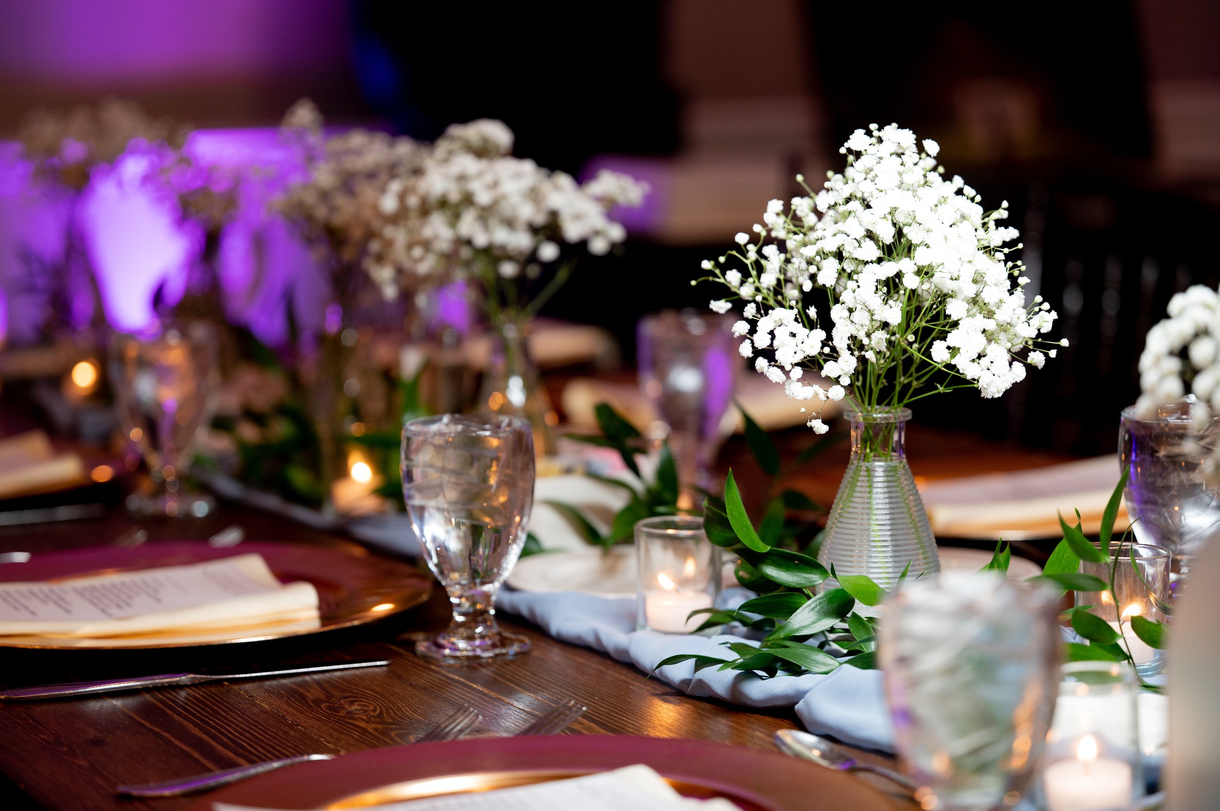 Decorated banquet table with floral centerpieces, candle lights, glassware, and plates for an event or celebration.