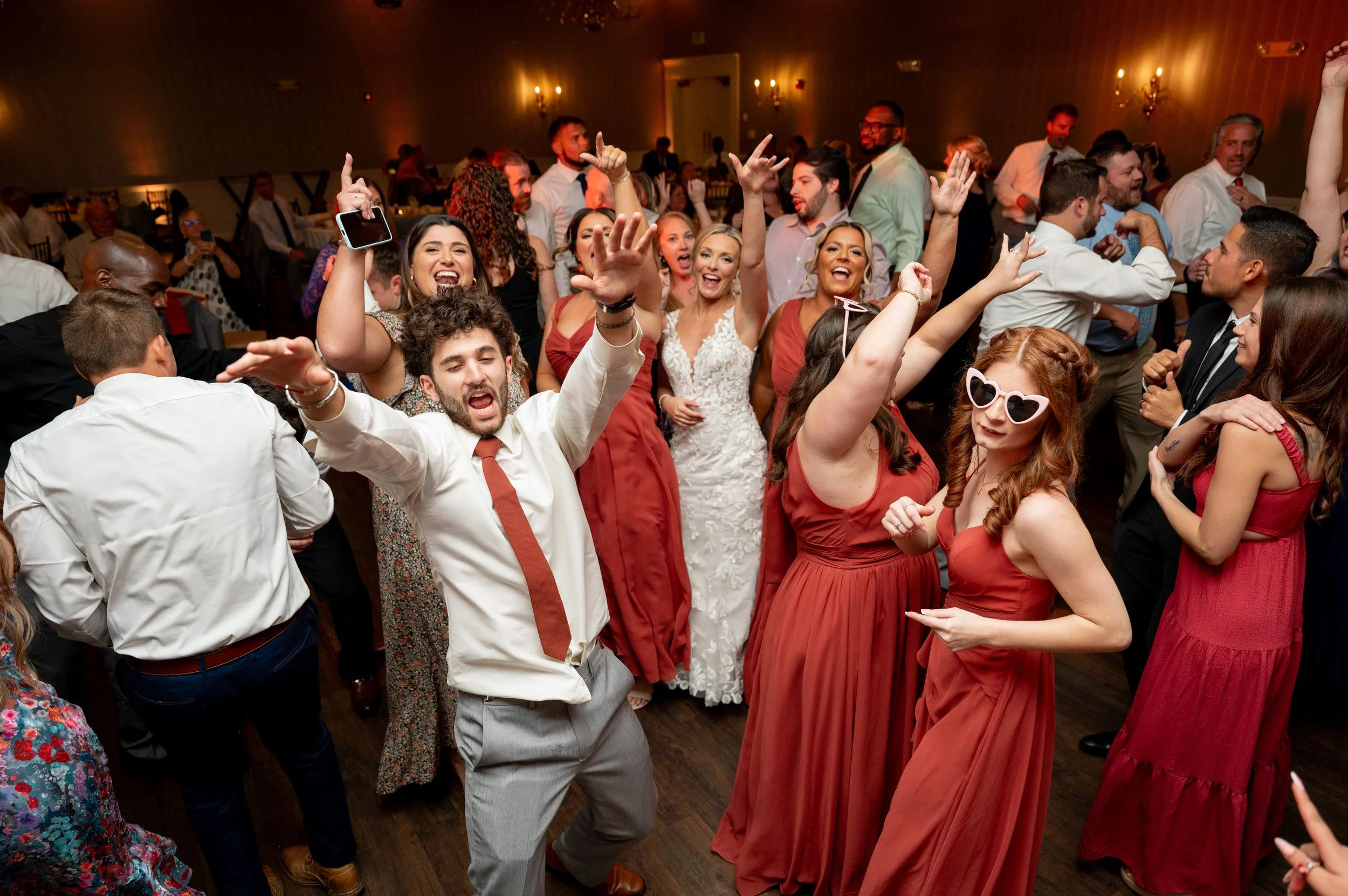 People dancing and celebrating at a wedding reception, with some wearing formal attire and others in casual clothes.