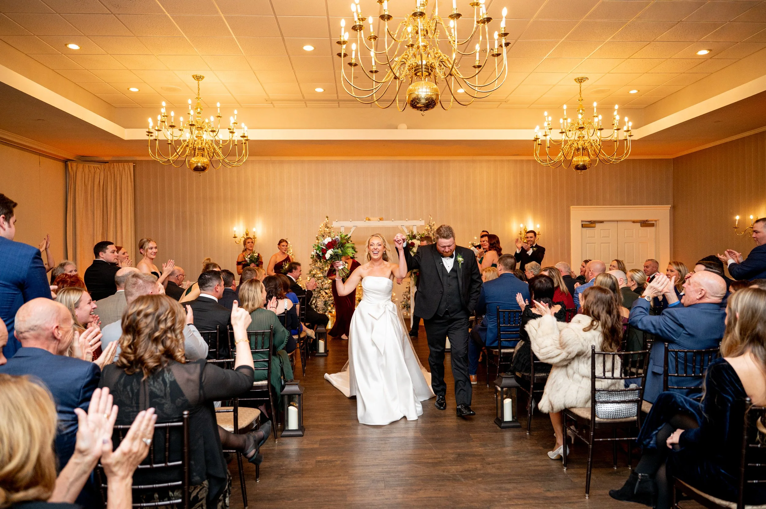 Bride and groom walking down the aisle after wedding ceremony in elegant venue with chandeliers, surrounded by applauding guests.