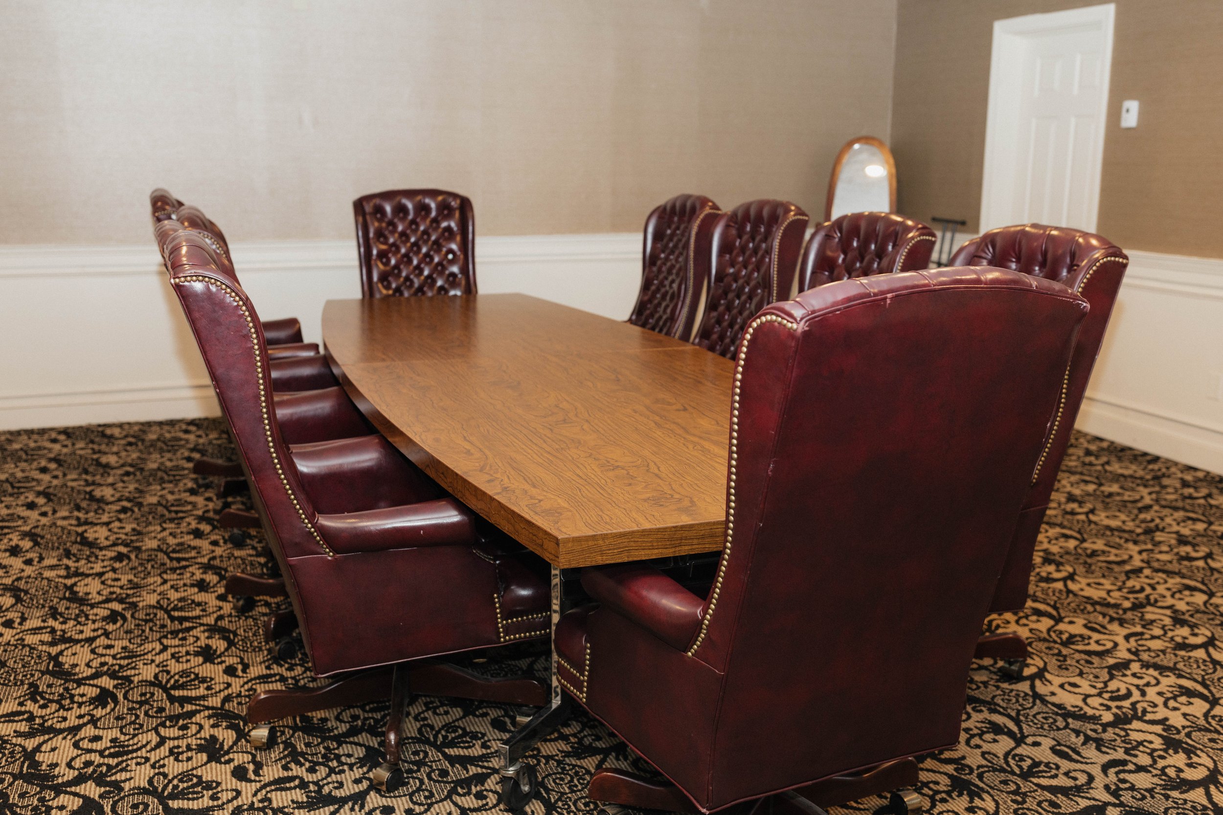 Empty conference room with a large wooden table and high-back leather chairs.