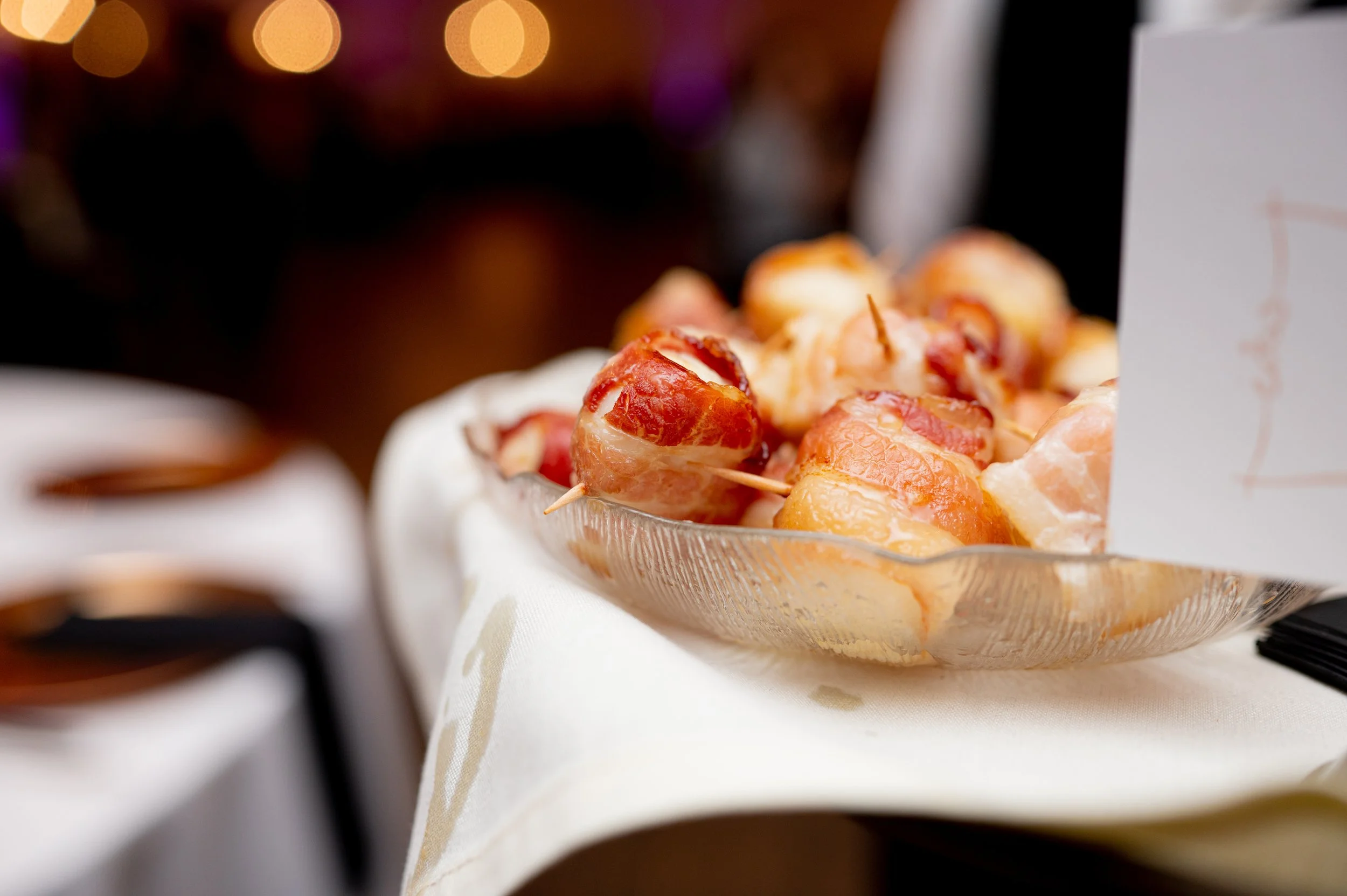 Bacon-wrapped appetizers on a glass plate at a festive event.