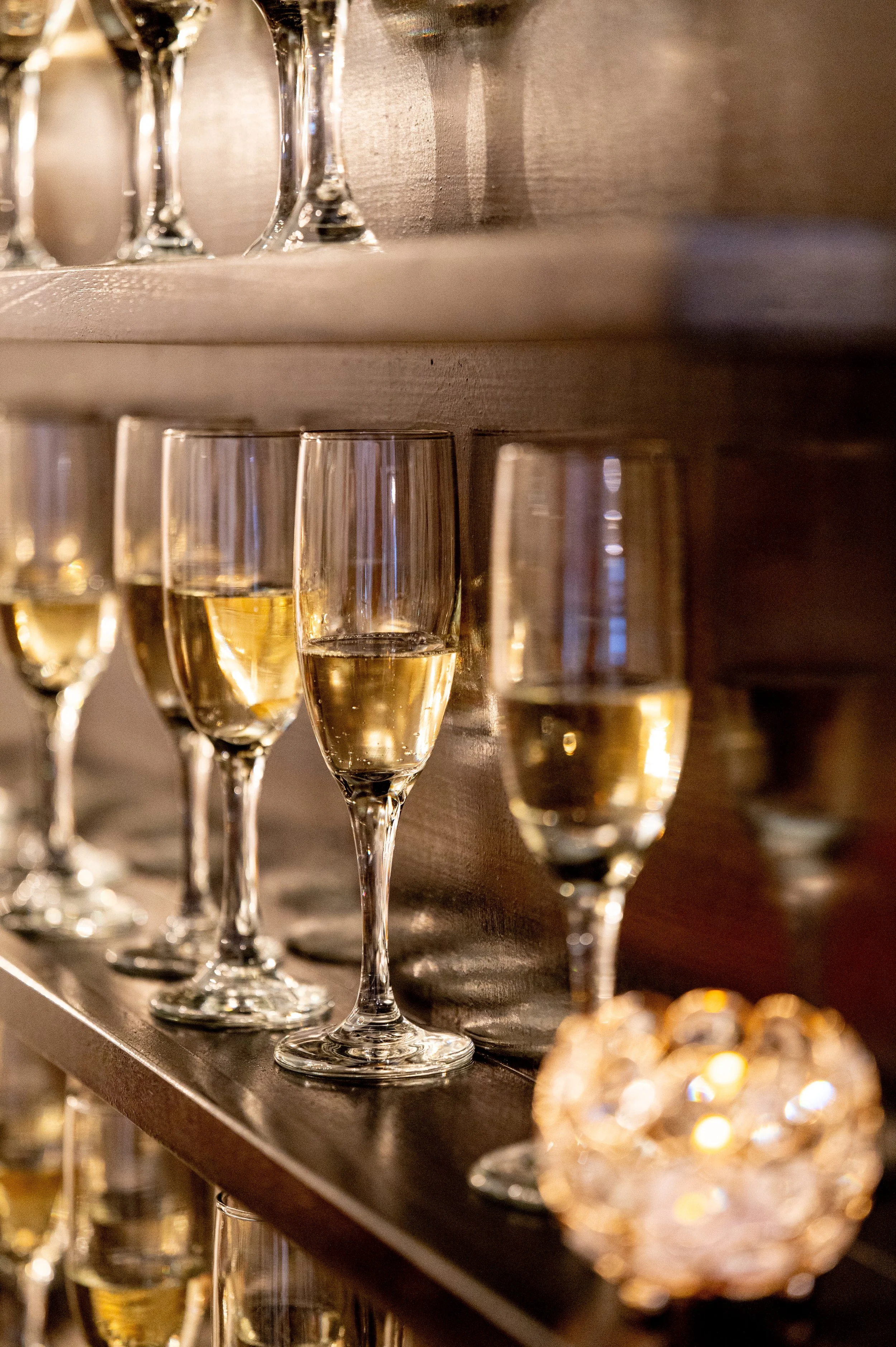 Several glasses of sparkling wine or champagne on a wooden shelf, with a decorative candle holder in the foreground.