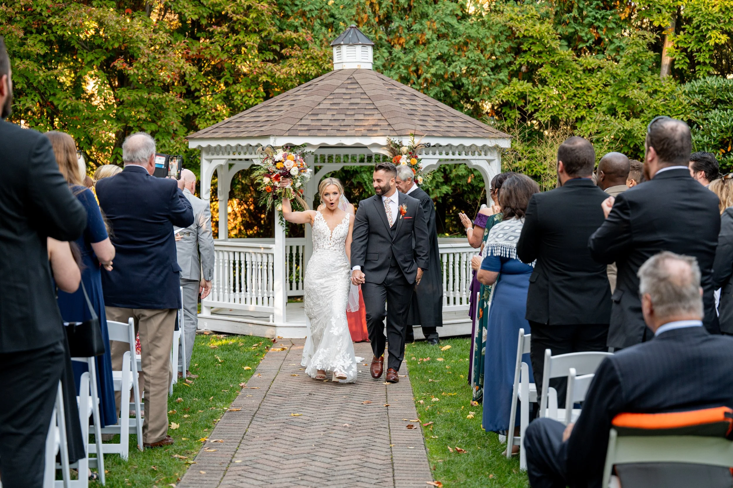 Bride and groom walking down the aisle after their wedding ceremony in an outdoor garden, with guests standing and taking photos.