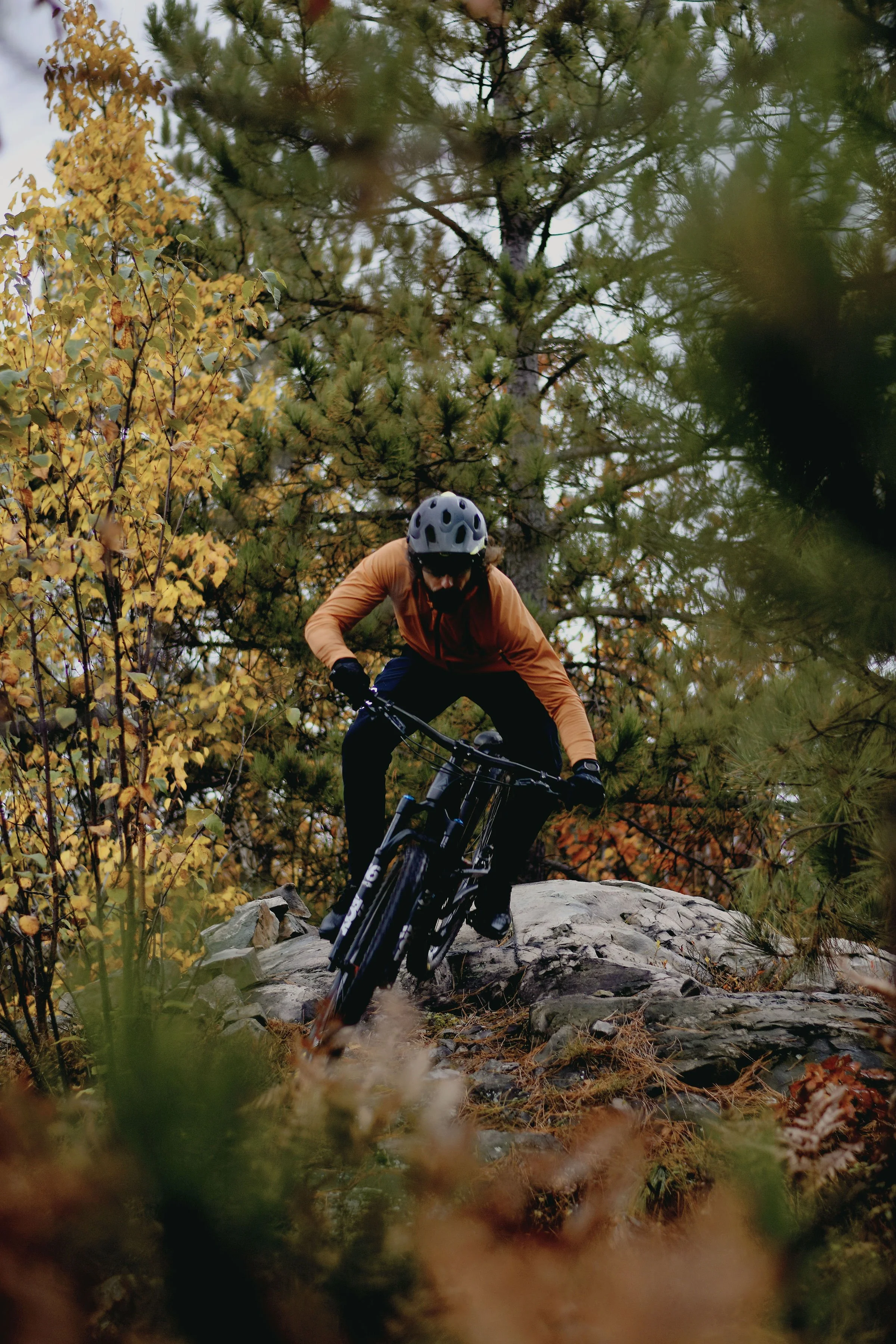 A person mountain biking on rocky terrain surrounded by fall foliage and trees.