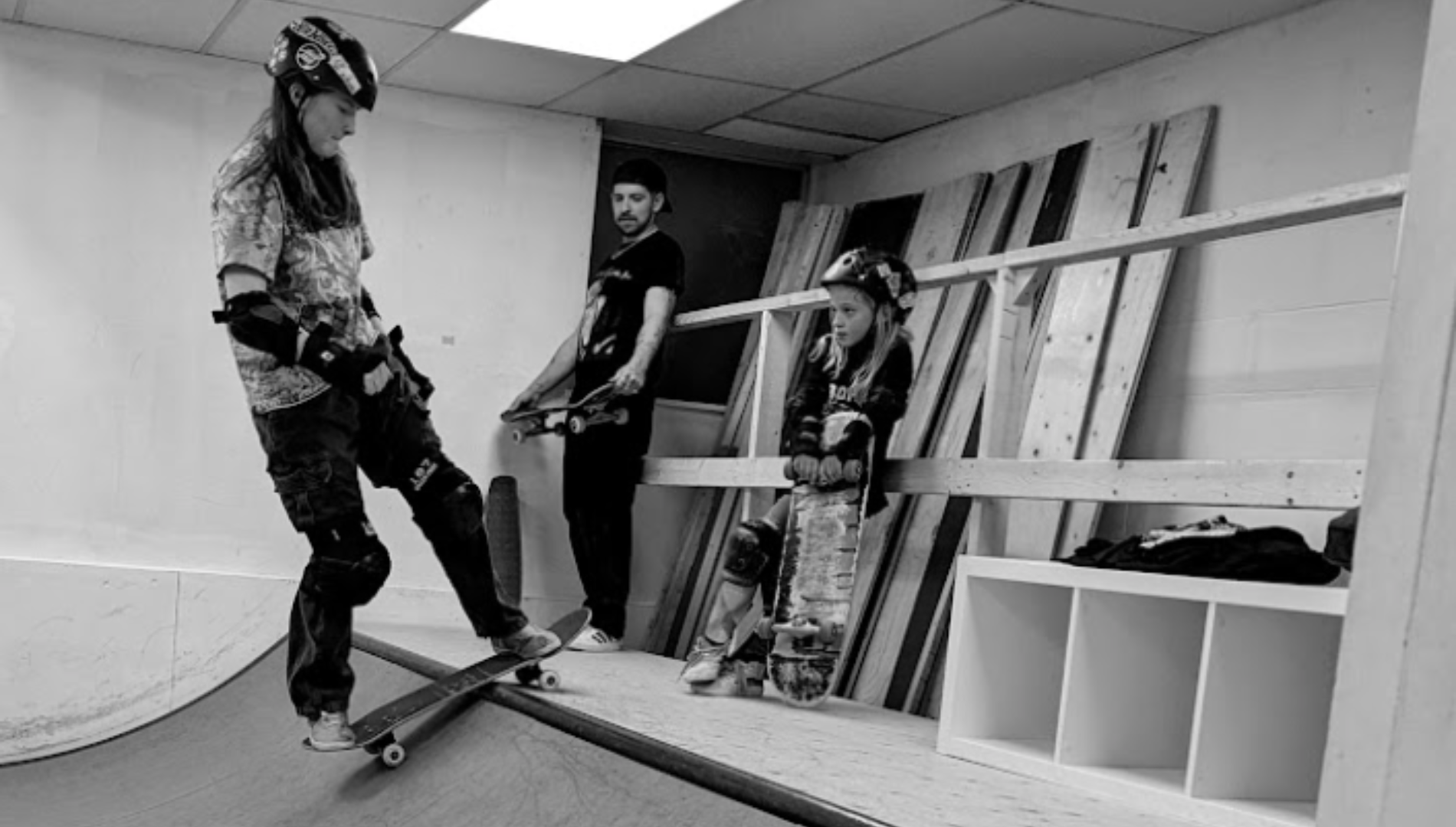 A girl wearing a helmet skateboarding on a ramp, with a girl and a man looking on in the background.