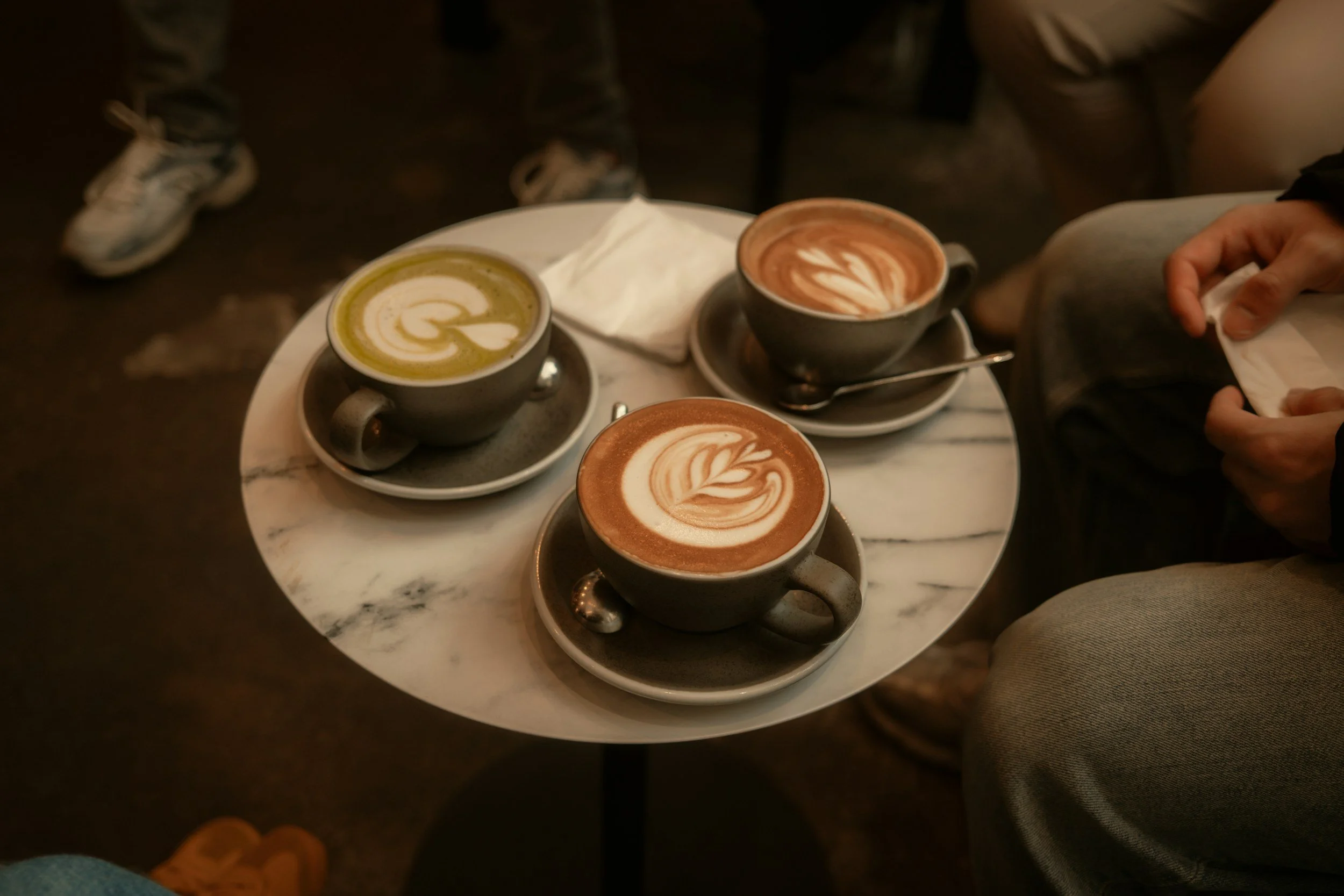 Three cups of coffee with latte art on a round marble table.