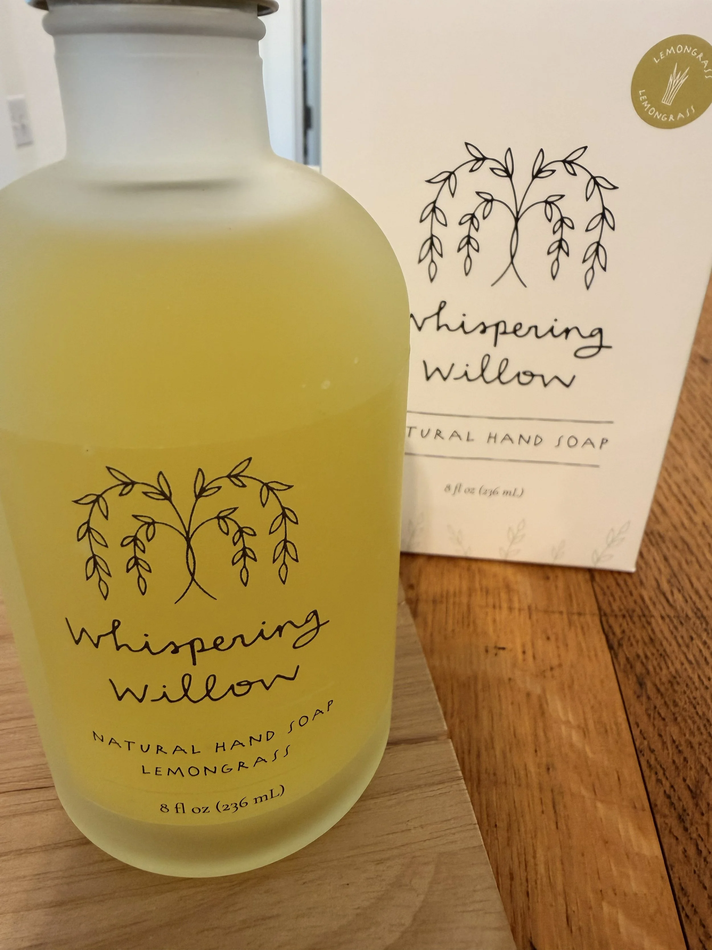 Close-up of Whispering Willow's Lemongrass Natural Pump Hand Soap on display with product box in background at Bloomie's Boutique