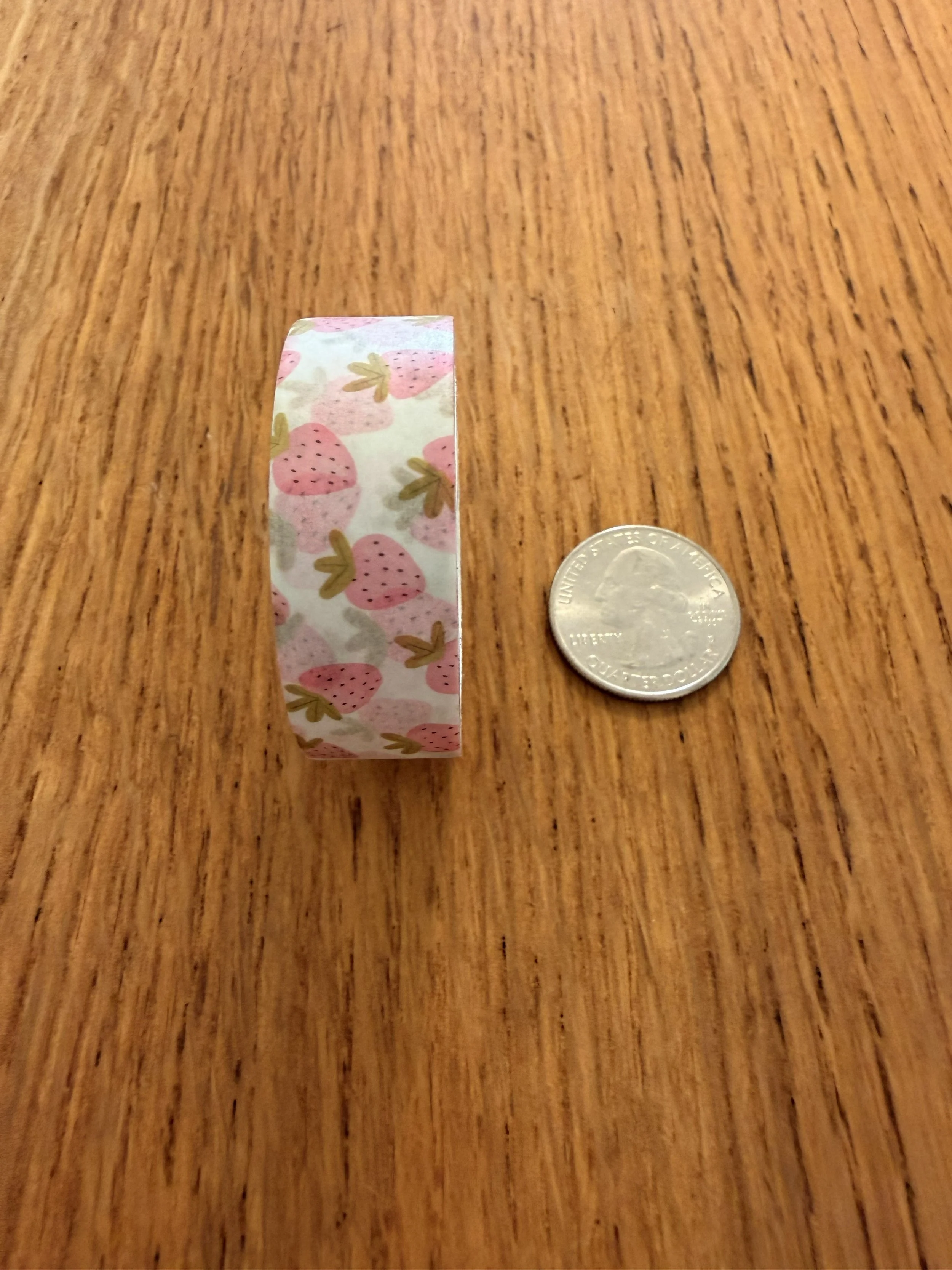 One roll of Ramona & Ruth's Strawberry Washi Tape on edge with quarter on wood countertop