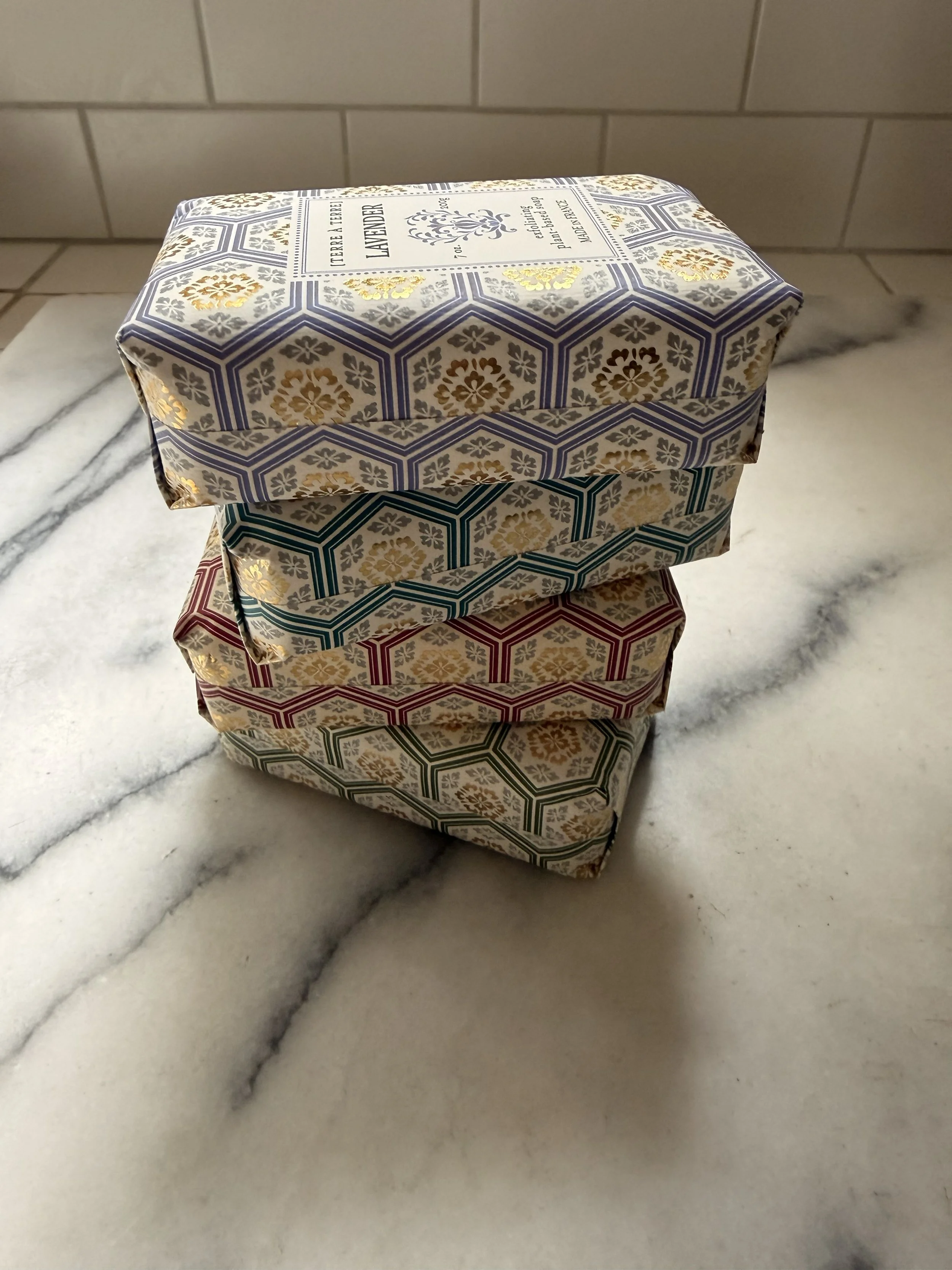 Stack of four different Terre á Terre soaps including Lavender, French Pear, Black Cherry, and Verbena on marble