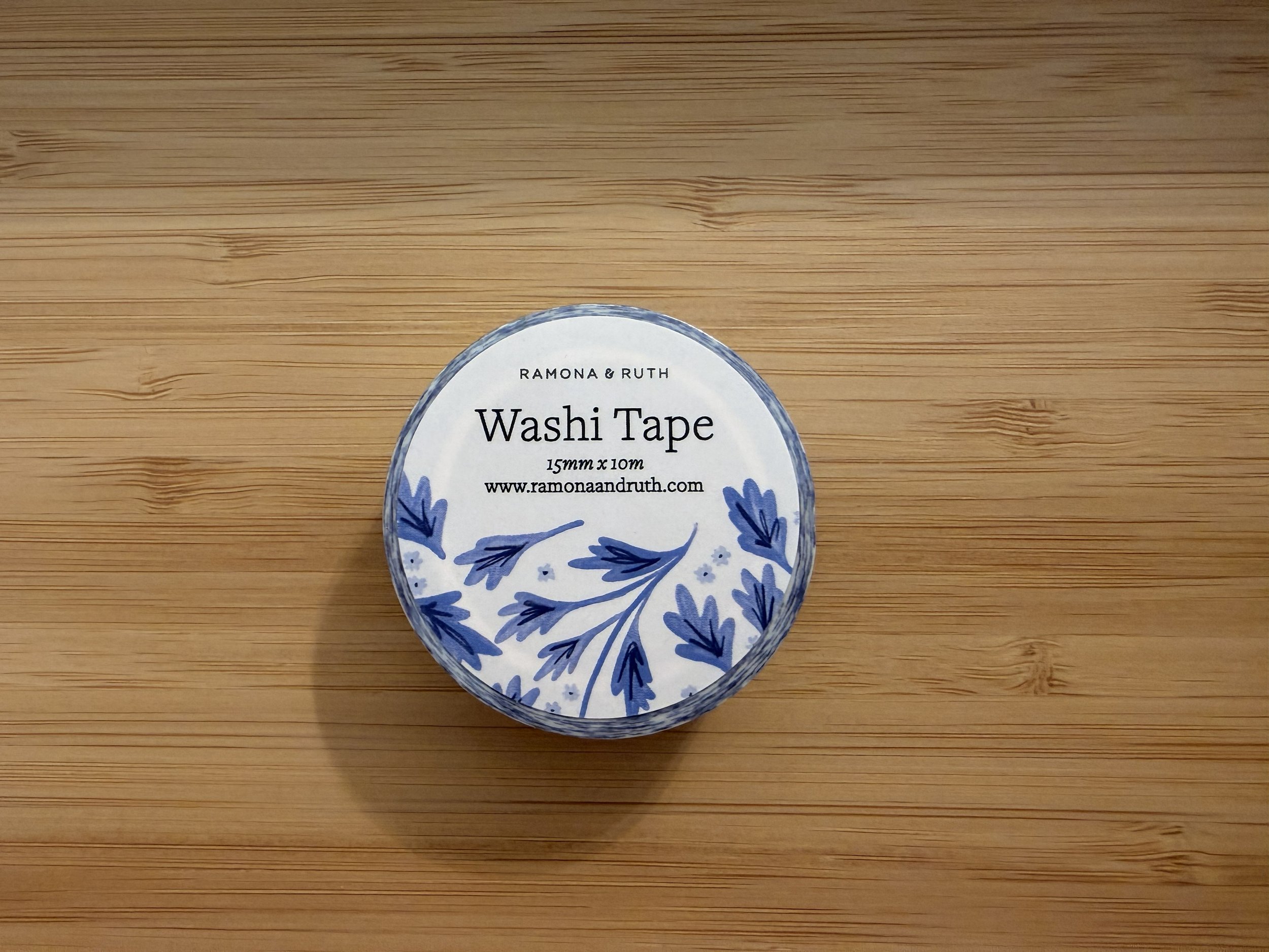 One roll of Ramona & Ruth's Blue Vines Washi Tape laying flat on bamboo