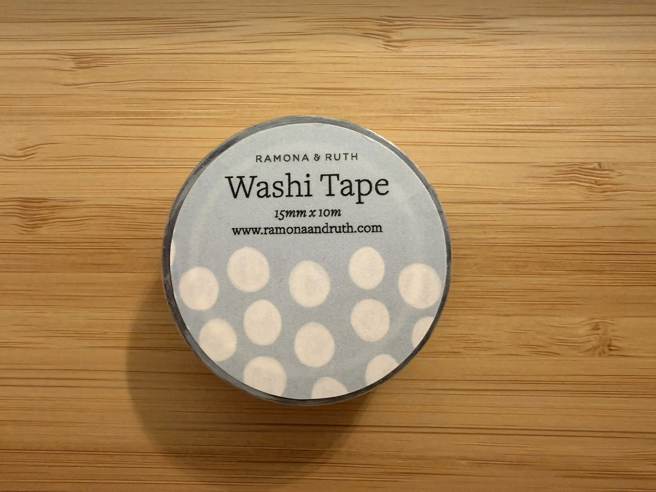 One roll of Ramona & Ruth's Soft Dots Washi Tape laying flat on bamboo