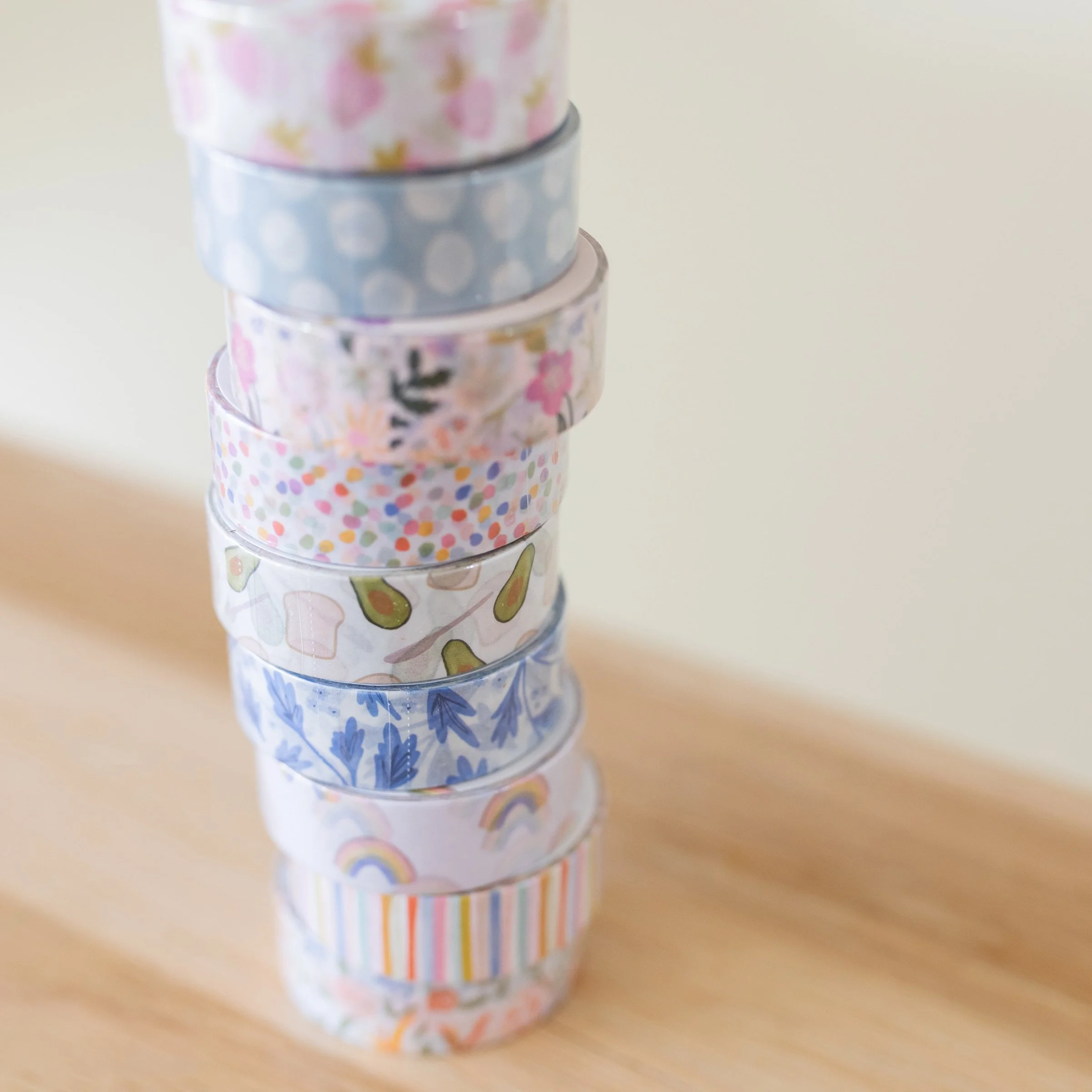 Several rolls of Ramona & Ruth's washi tape stacked on wood counter including Rainbows Washi Tape, among others