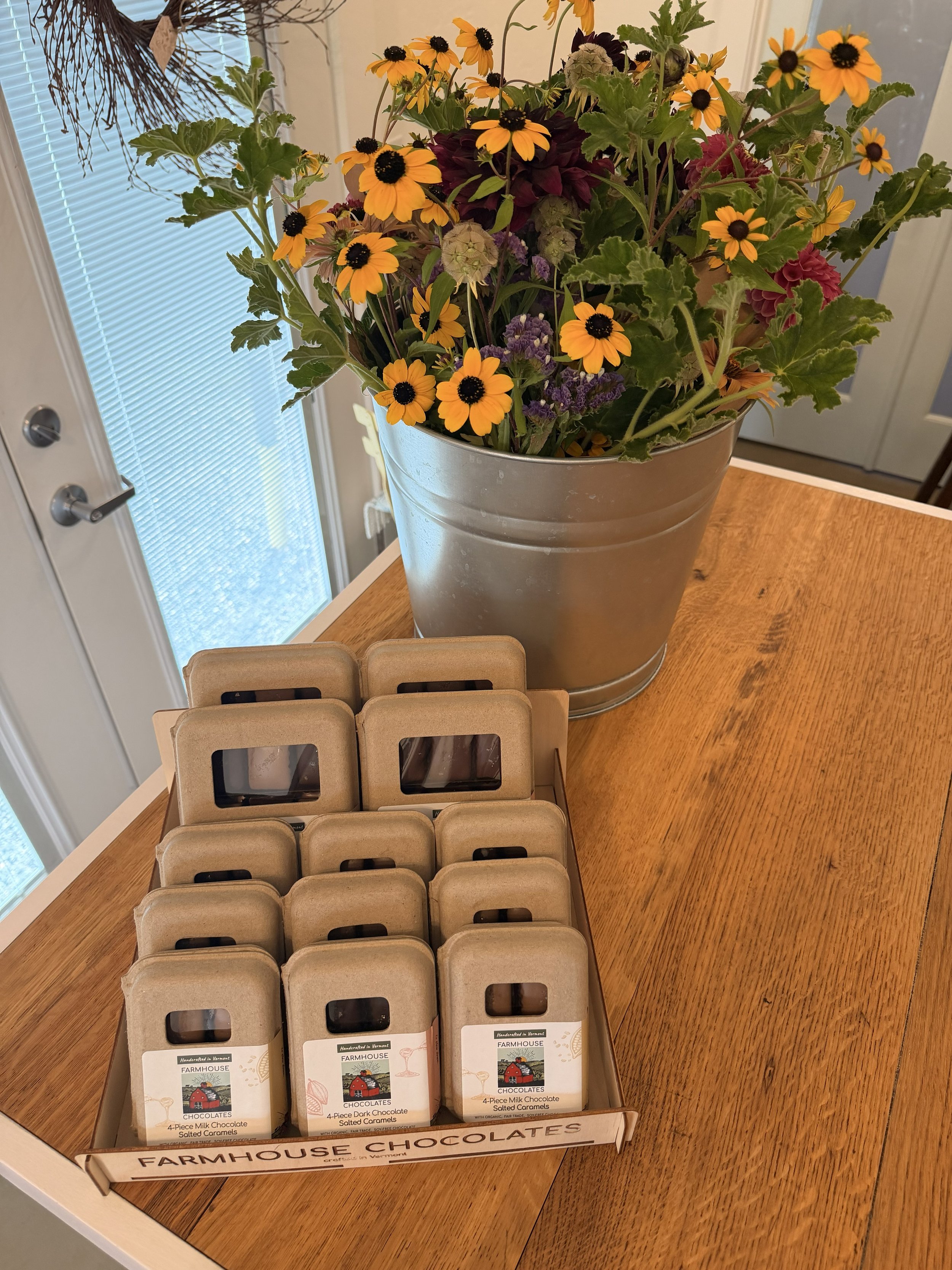 Display of Farmhouse Chocolates' 9-Piece Dark Chocolate Salted Caramels and more with flowers on wood countertop